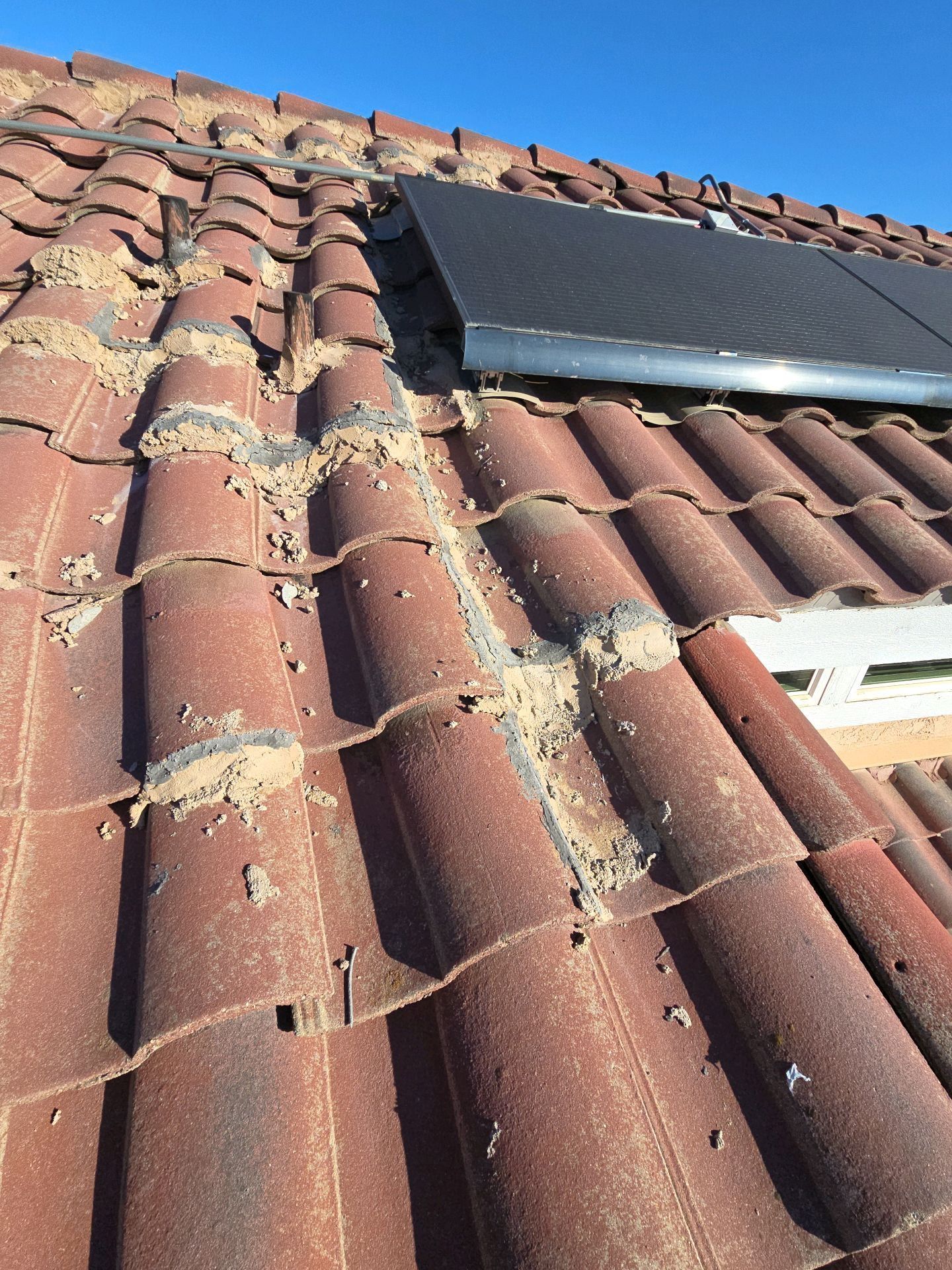 A damaged tiled roof with crumbling mortar joints visible between sections and a dark solar panel in the upper corner.