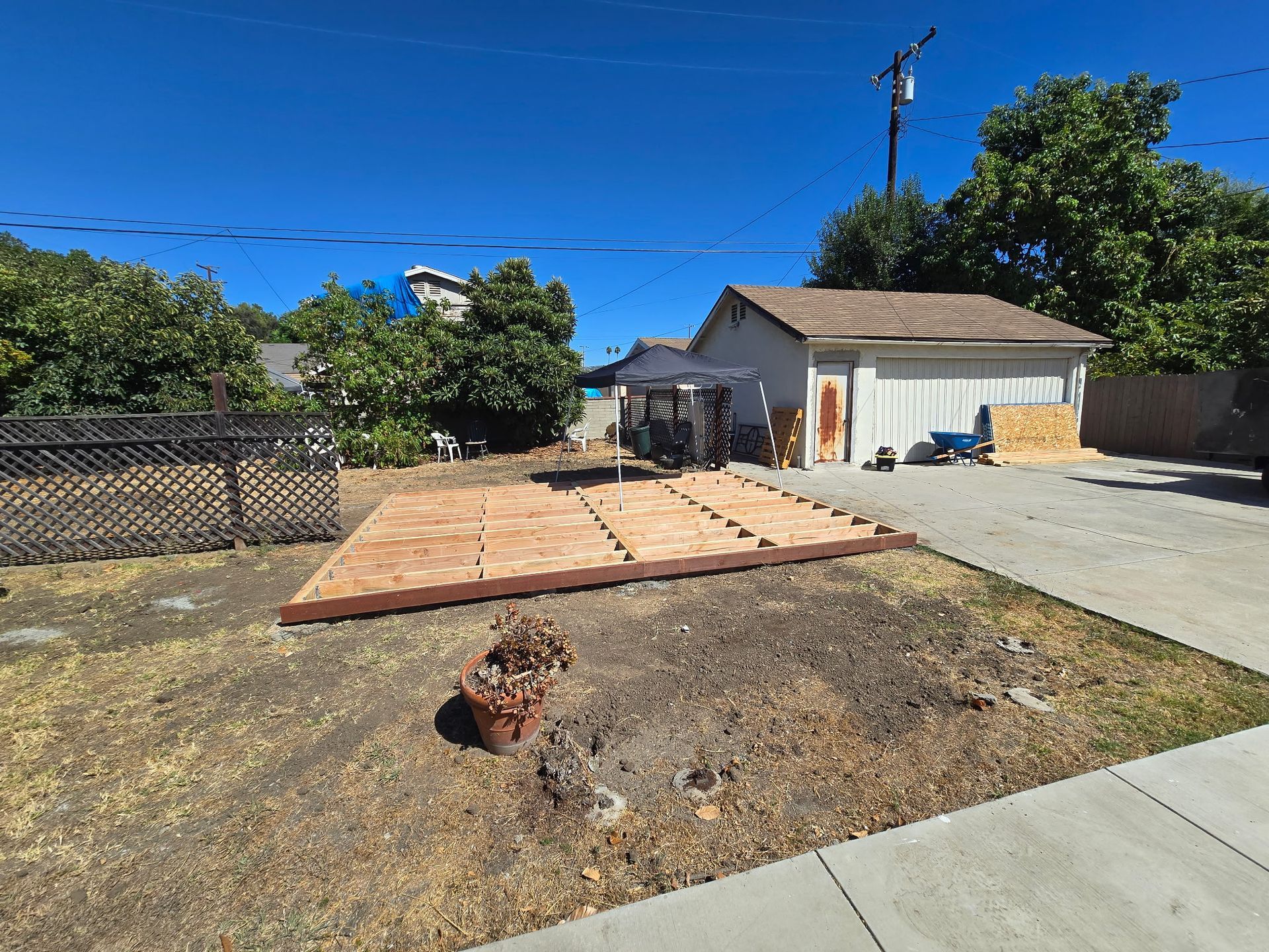 Backyard with patio pavers, a driveway, garage, and trees under a clear blue sky