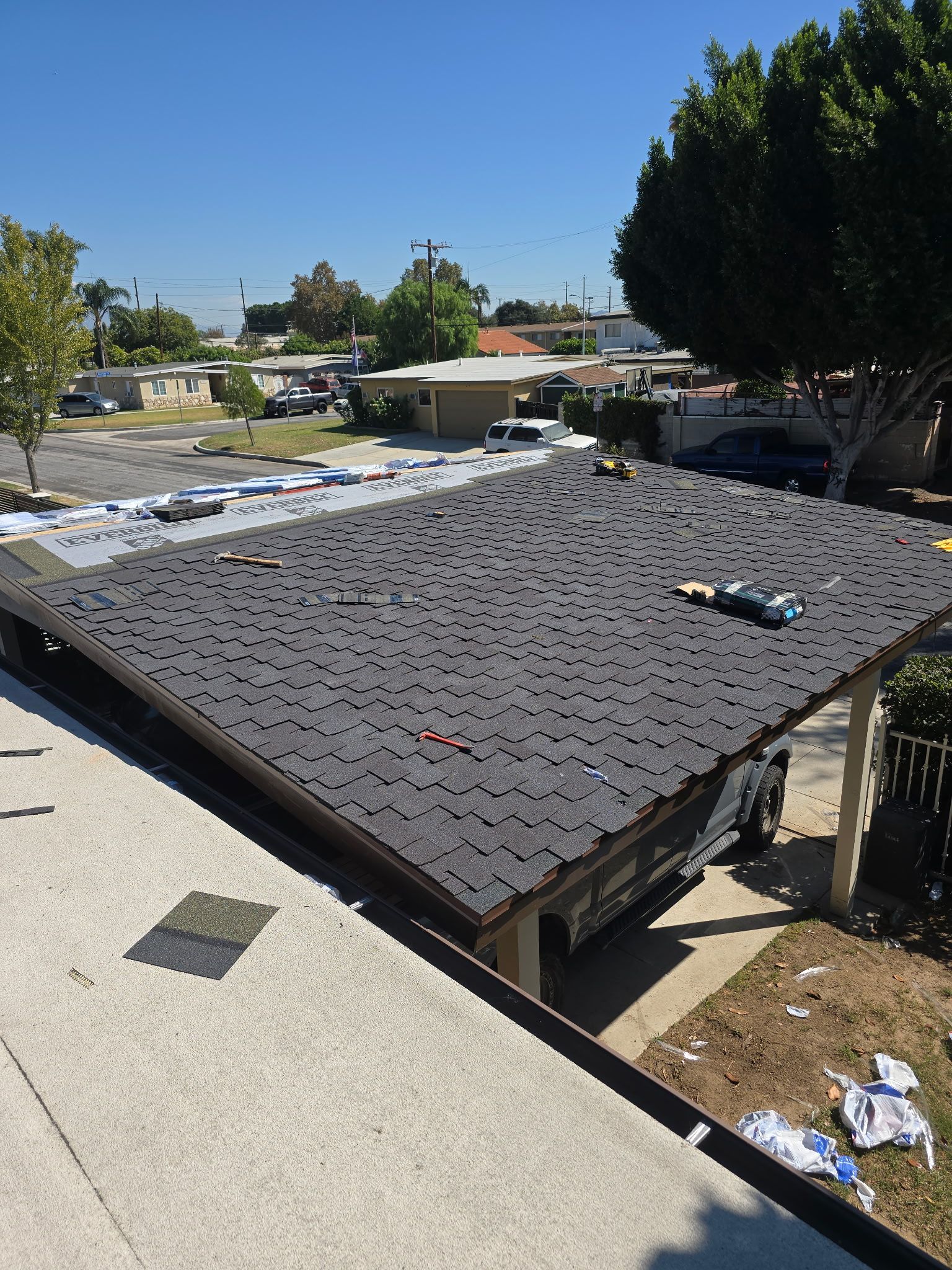 Rooftop covered with dark solar panels in a suburban neighborhood under a clear blue sky