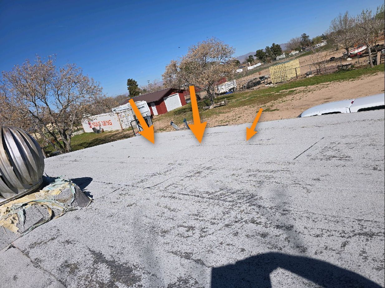 A roof with weathered, grey coating and three orange arrows pointing to areas of surface wear and peeling.