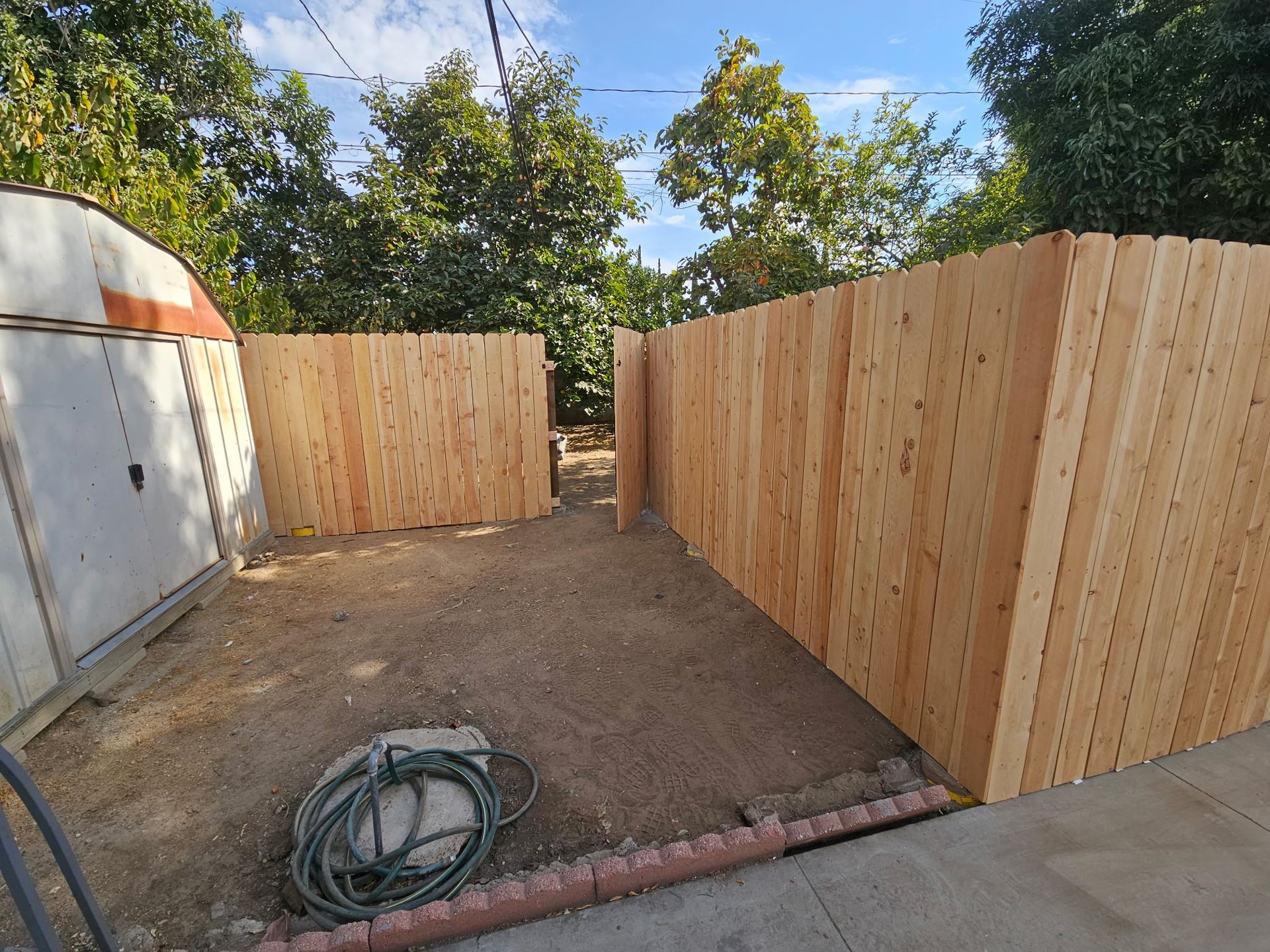Newly installed wooden privacy fence panels enclosing a dirt yard next to a shed.