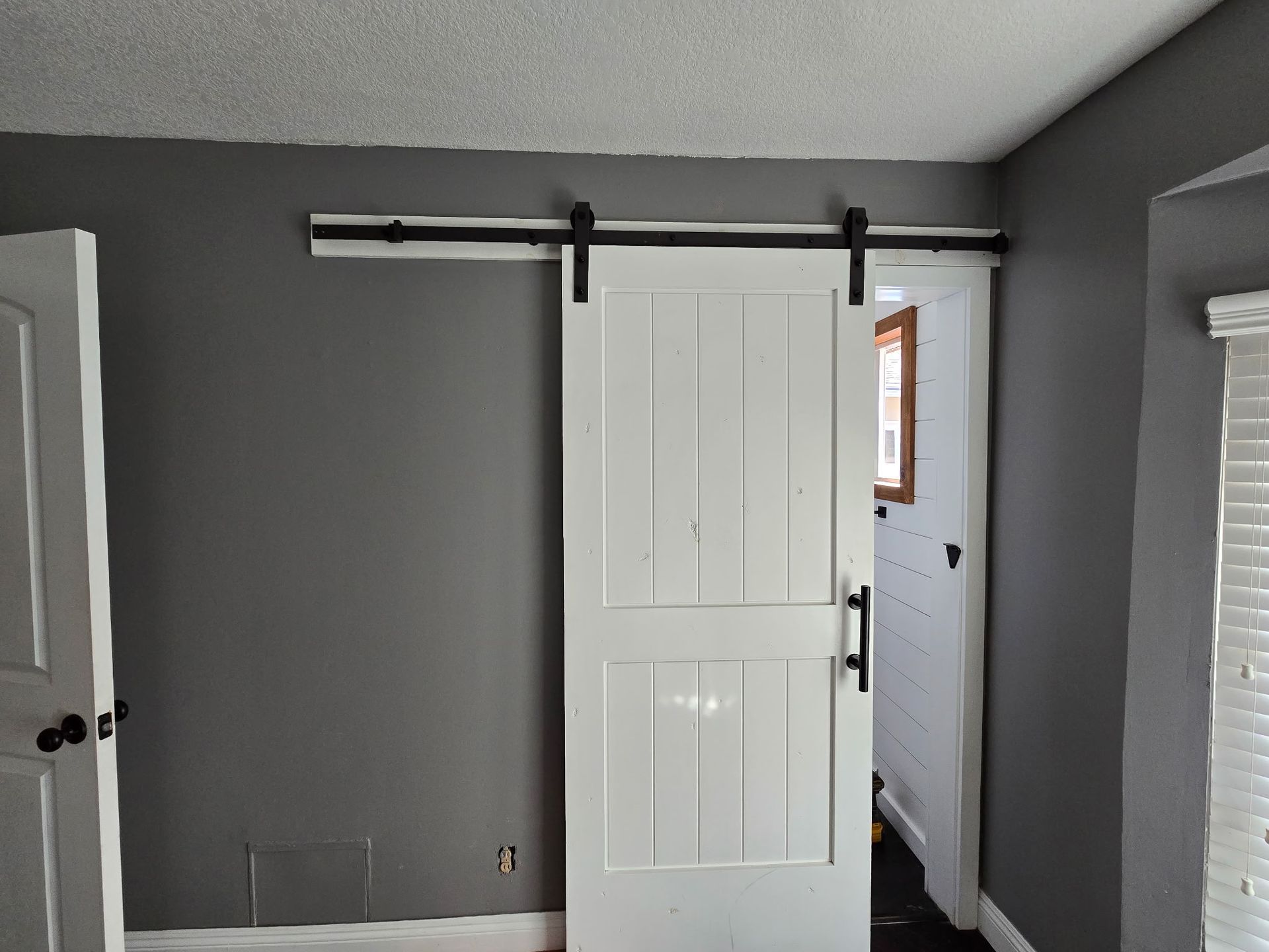 A white barn door with black hardware installed on a gray wall in a room.