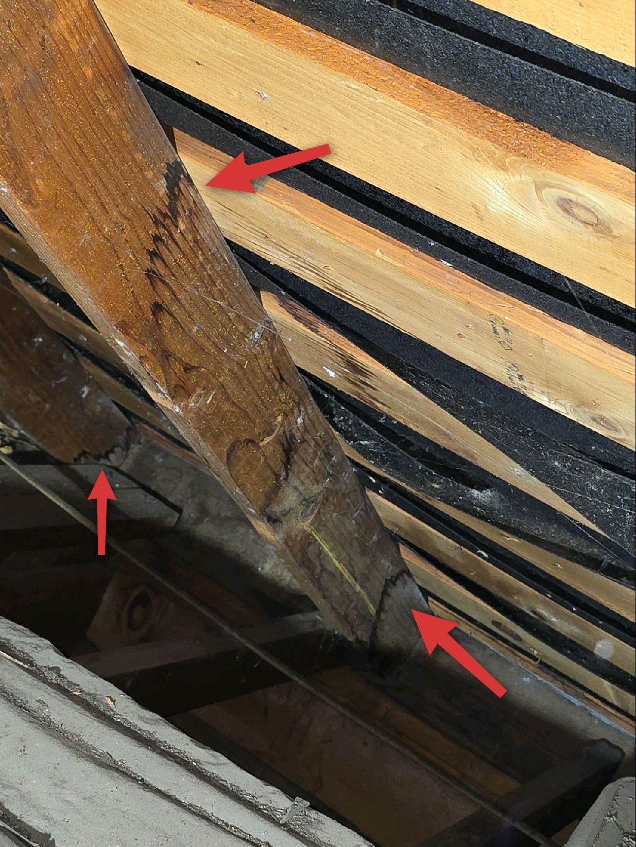A wooden rafter in an attic, marked with three red arrows highlighting points along its structure and joints.
