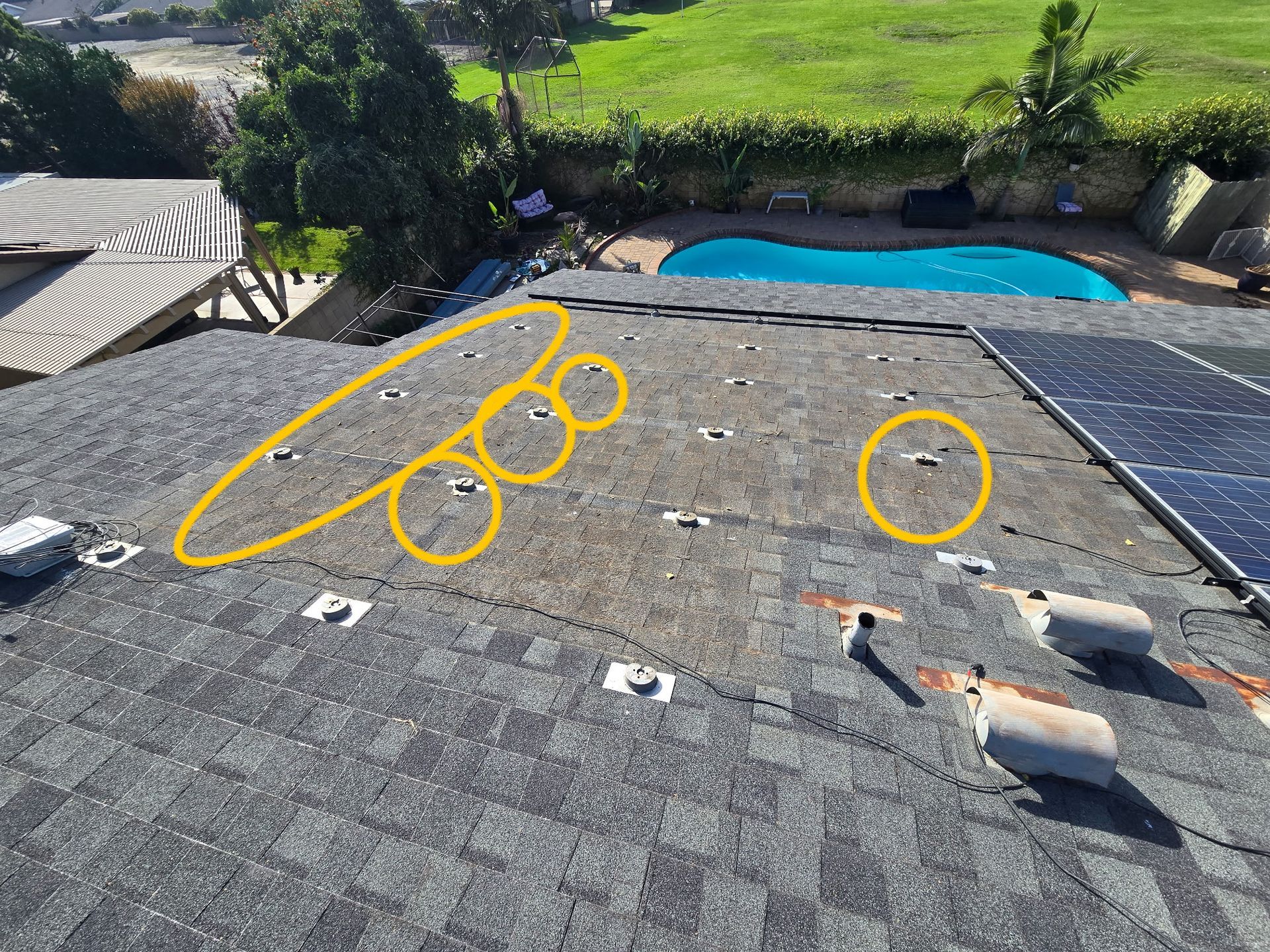 An aerial view of a shingled roof with several mounting brackets installed, some highlighted with yellow circles.