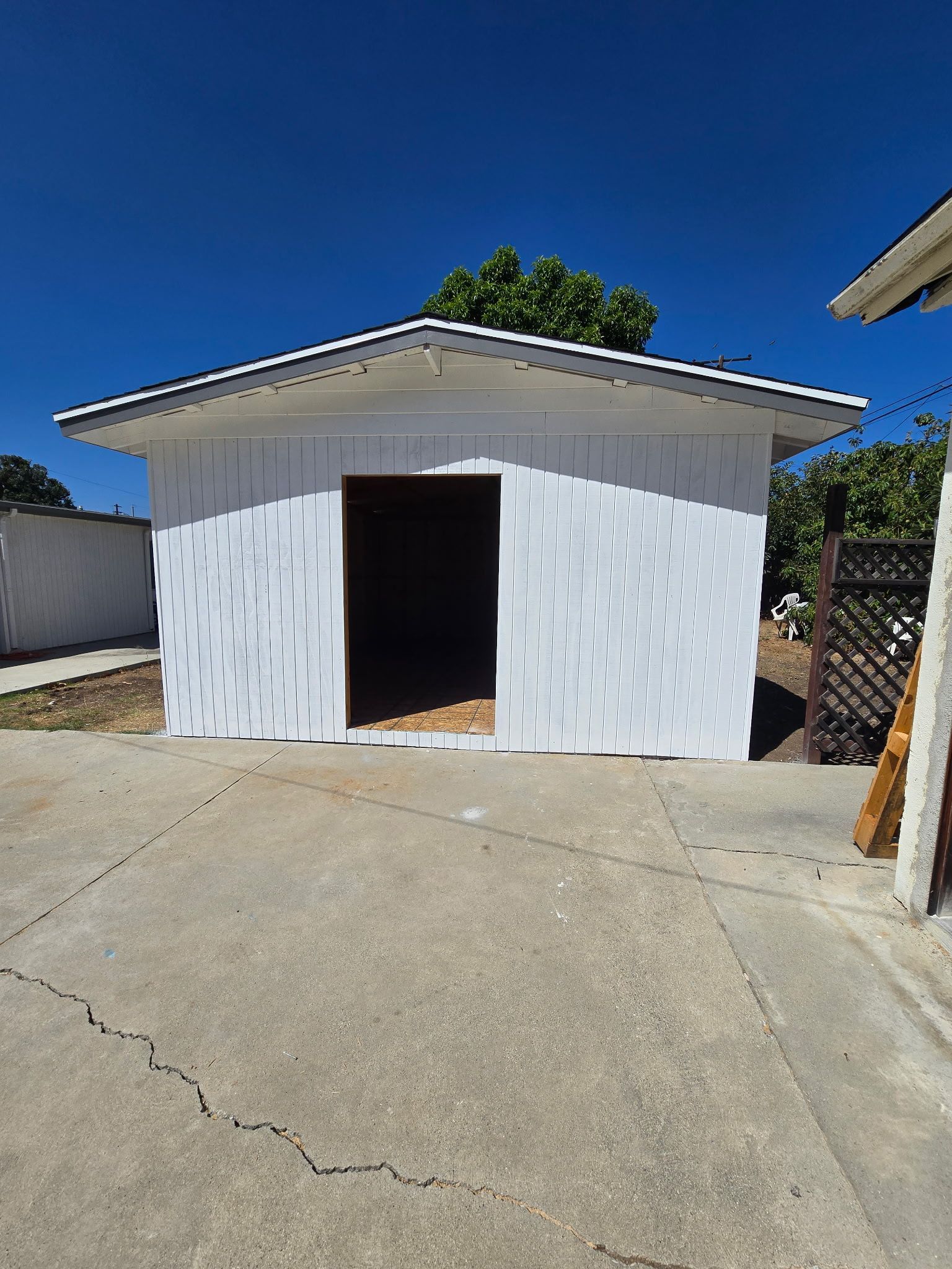 White garage/shed with open door on a sunny concrete driveway under a blue sky.