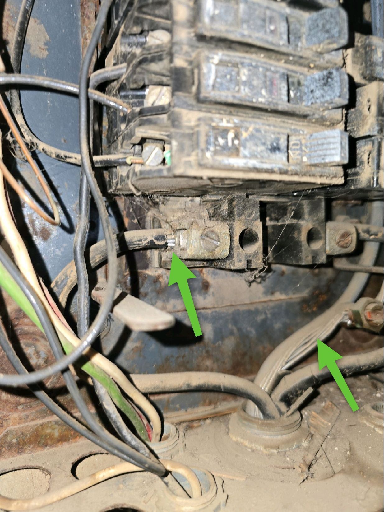 An electrical panel interior with green arrows pointing to specific wire connections and grounding terminals.