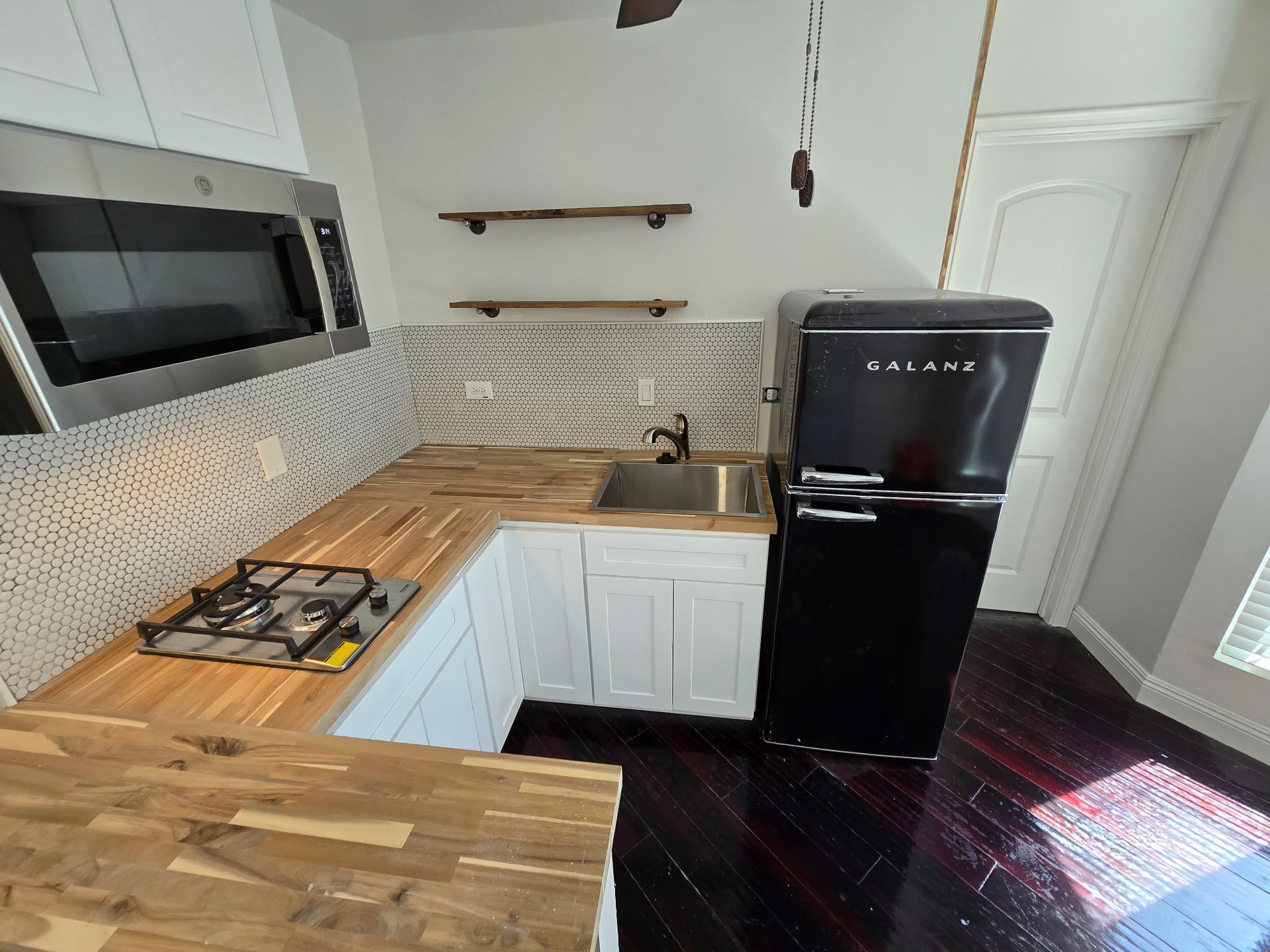 A small kitchen with white cabinets, wood countertops, a stainless steel gas cooktop, and a black retro-style refrigerator.