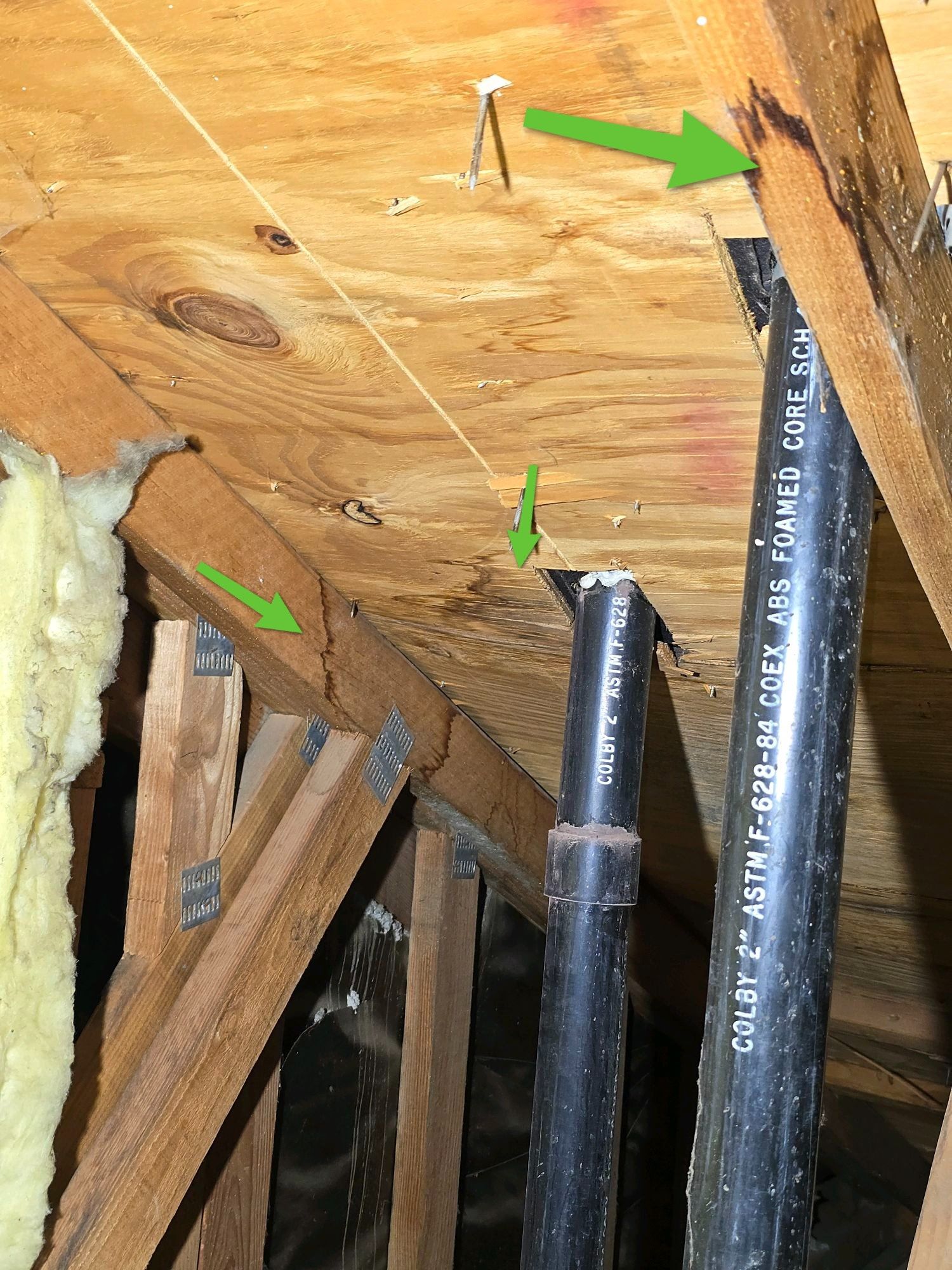 Attic view of roof deck water staining around plumbing vent pipes, with green arrows pointing to the affected areas.
