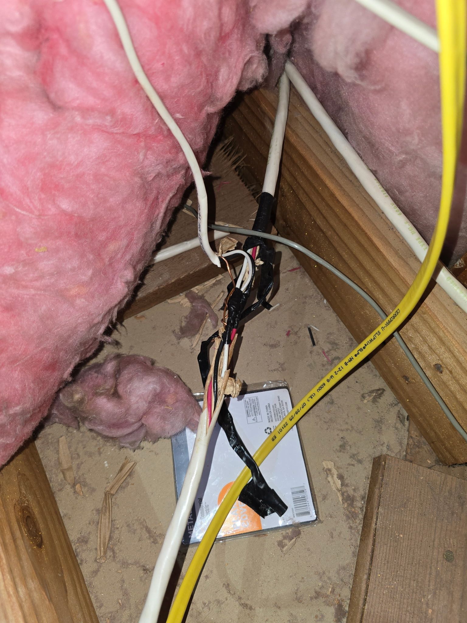 Unsafe exposed electrical wire splice wrapped in black electrical tape, sitting in an attic near wooden beams and insulation.