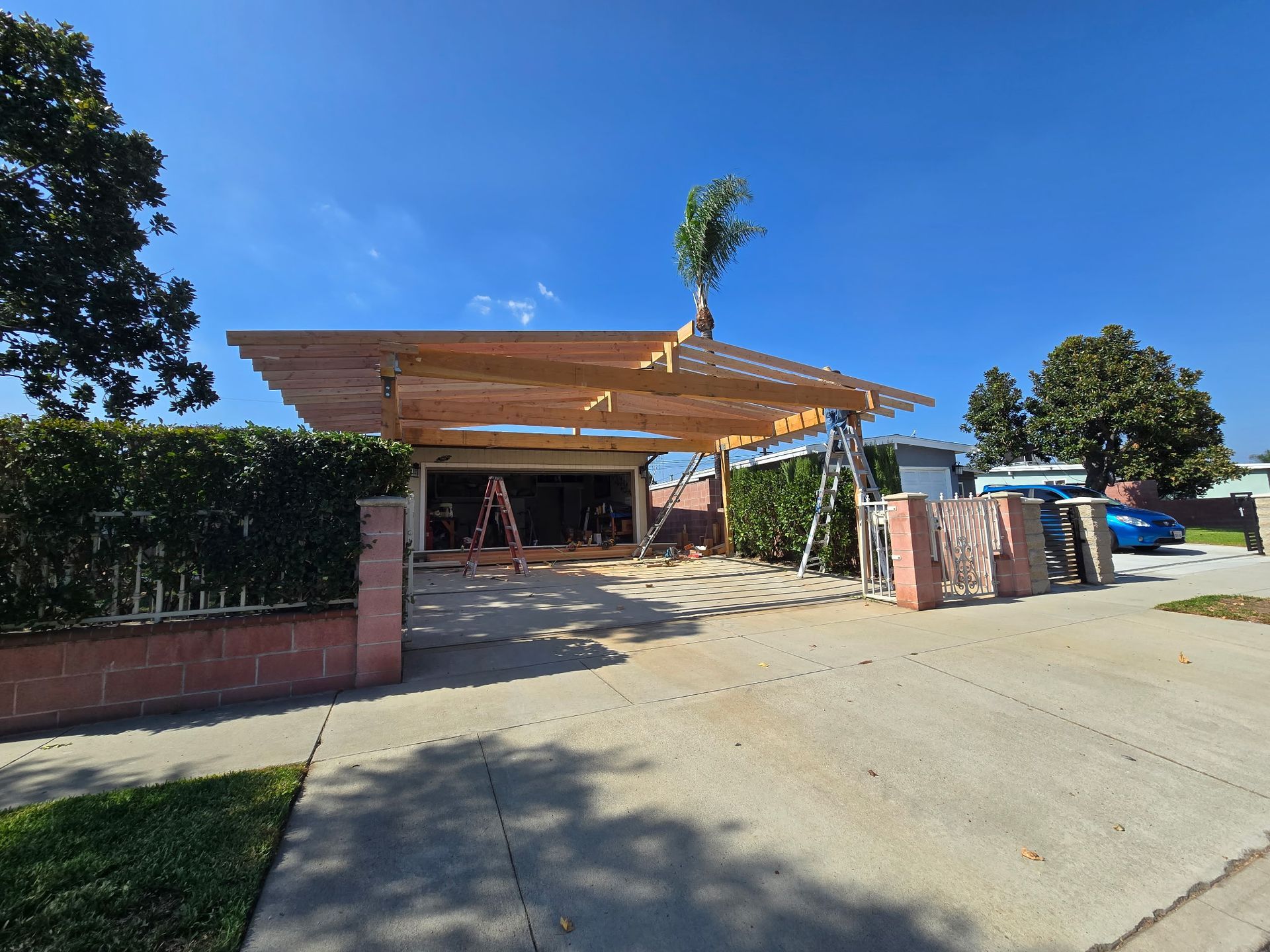 Open carport with a slanted wooden roof beside a driveway under a clear blue sky