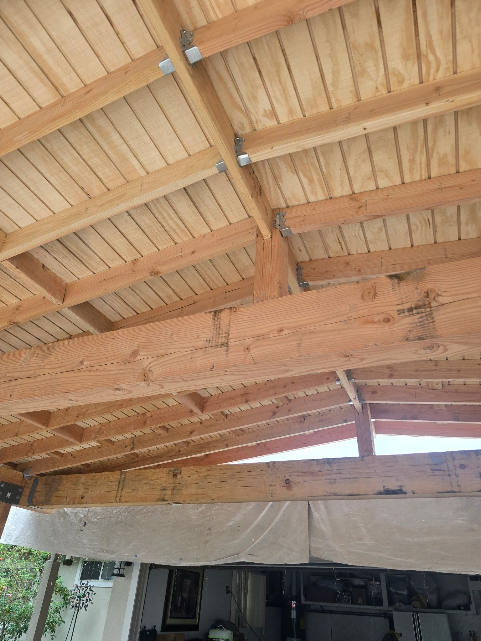 Wooden roof beams and slatted ceiling of a carport, with an opening showing a garage below.