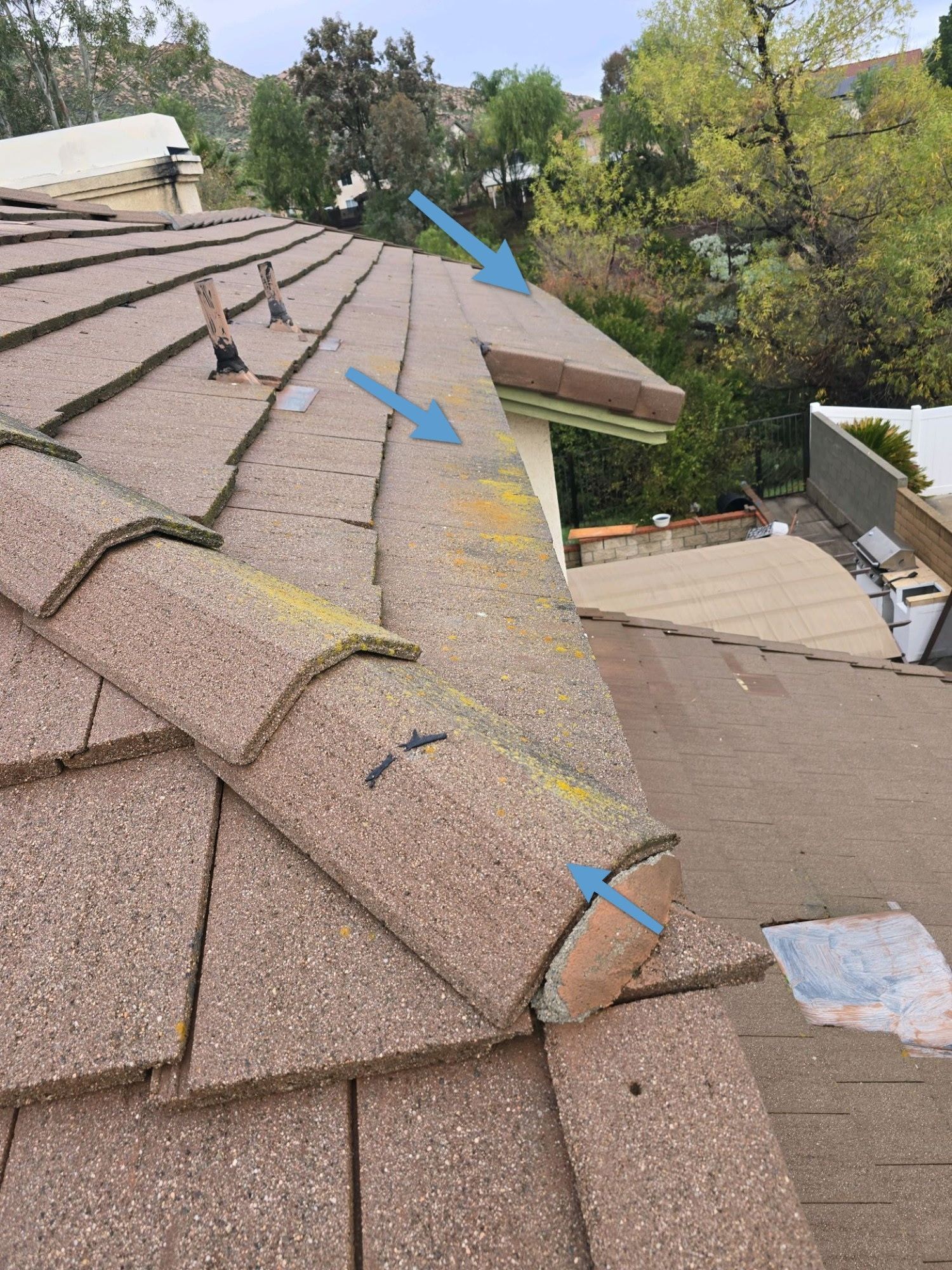 A brown concrete tile roof with blue arrows pointing to edge damage and missing mortar caps along the rake.