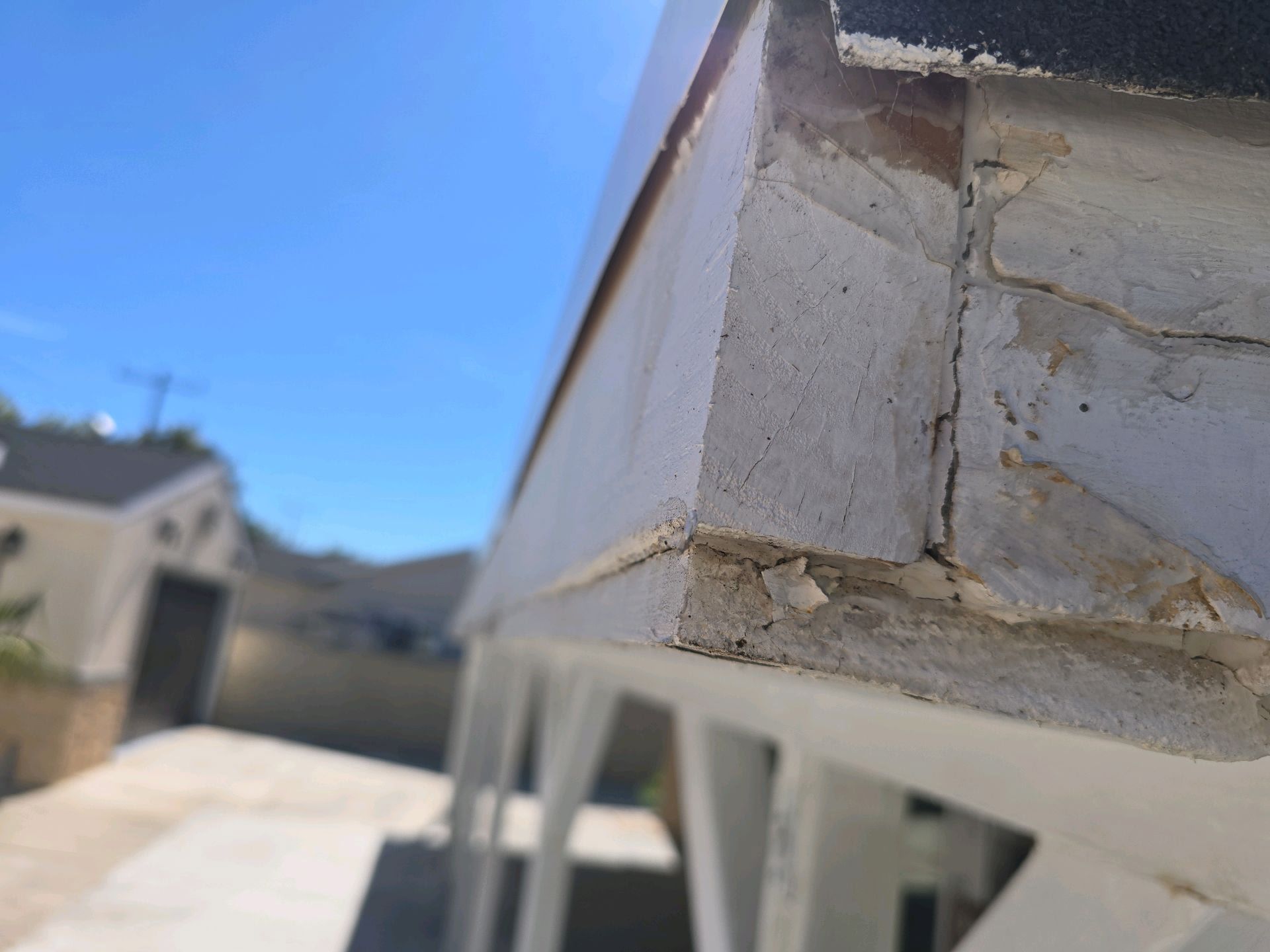 A close-up of a weathered, painted wooden roof eave edge with visible cracks and peeling paint on a sunny day.