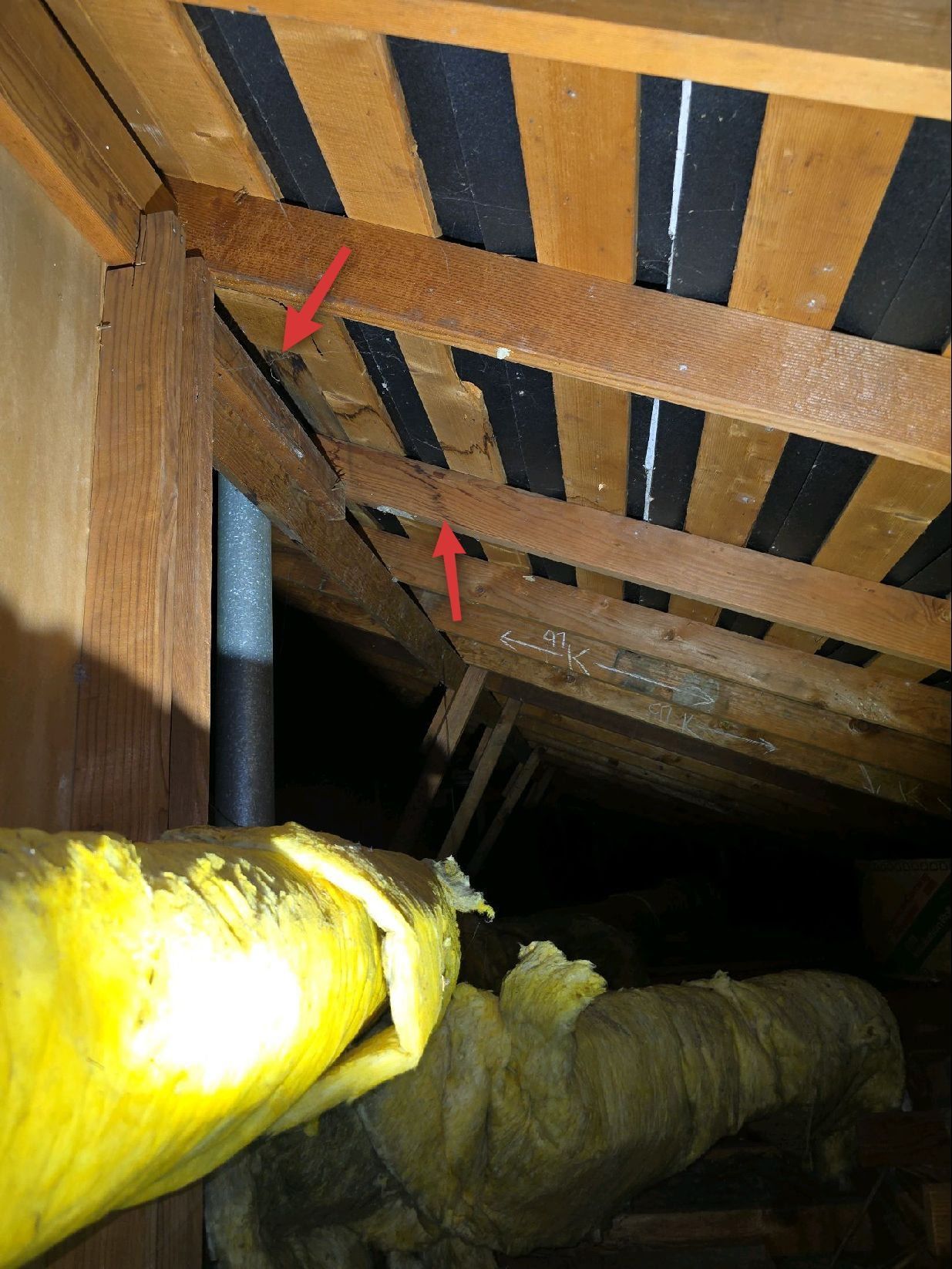 Attic view showing wooden rafters and black roof lining, with red arrows pointing to gaps in the structure.