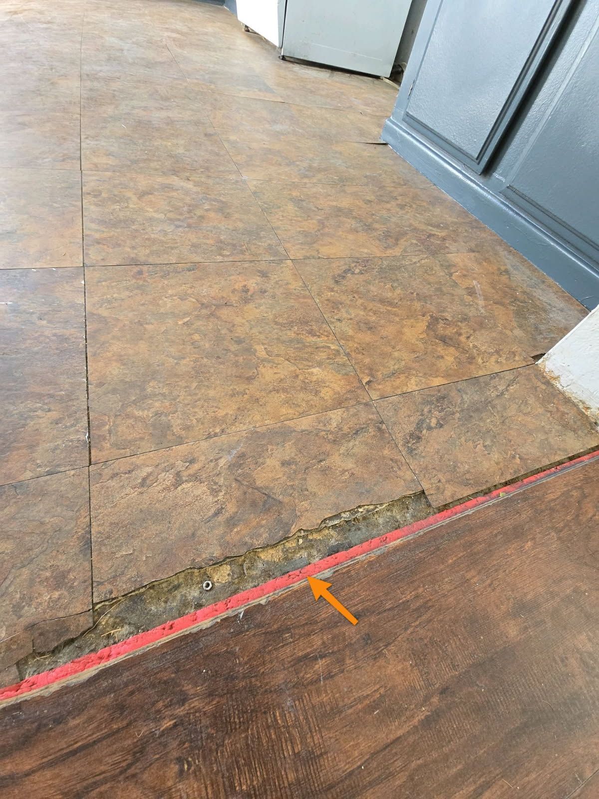 A transition strip between brown tile and wood-look flooring with a gap and an orange arrow pointing to the edge.