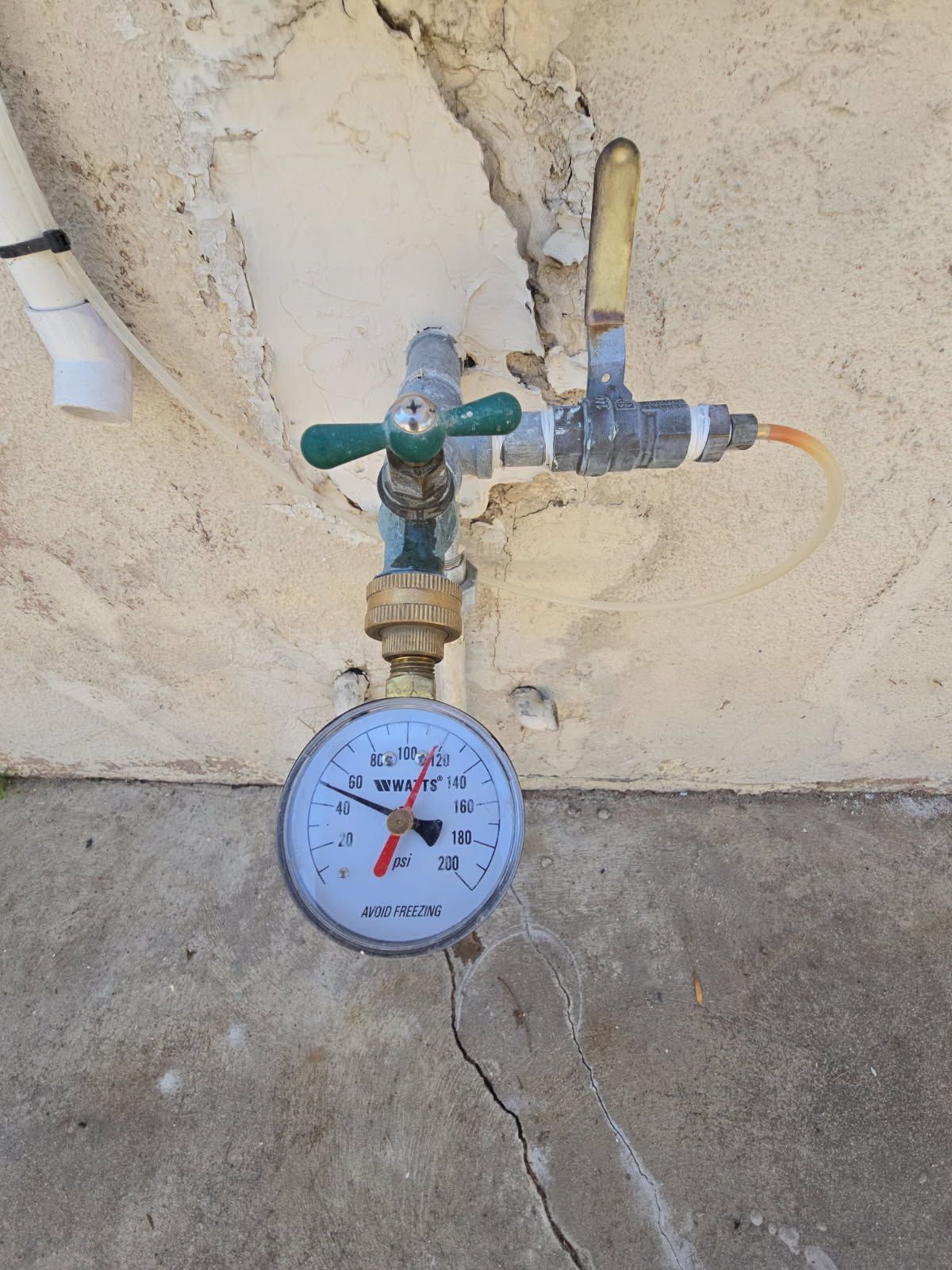 A pressure gauge attached to an outdoor water spigot shows a reading of approximately 45 psi on a concrete wall.