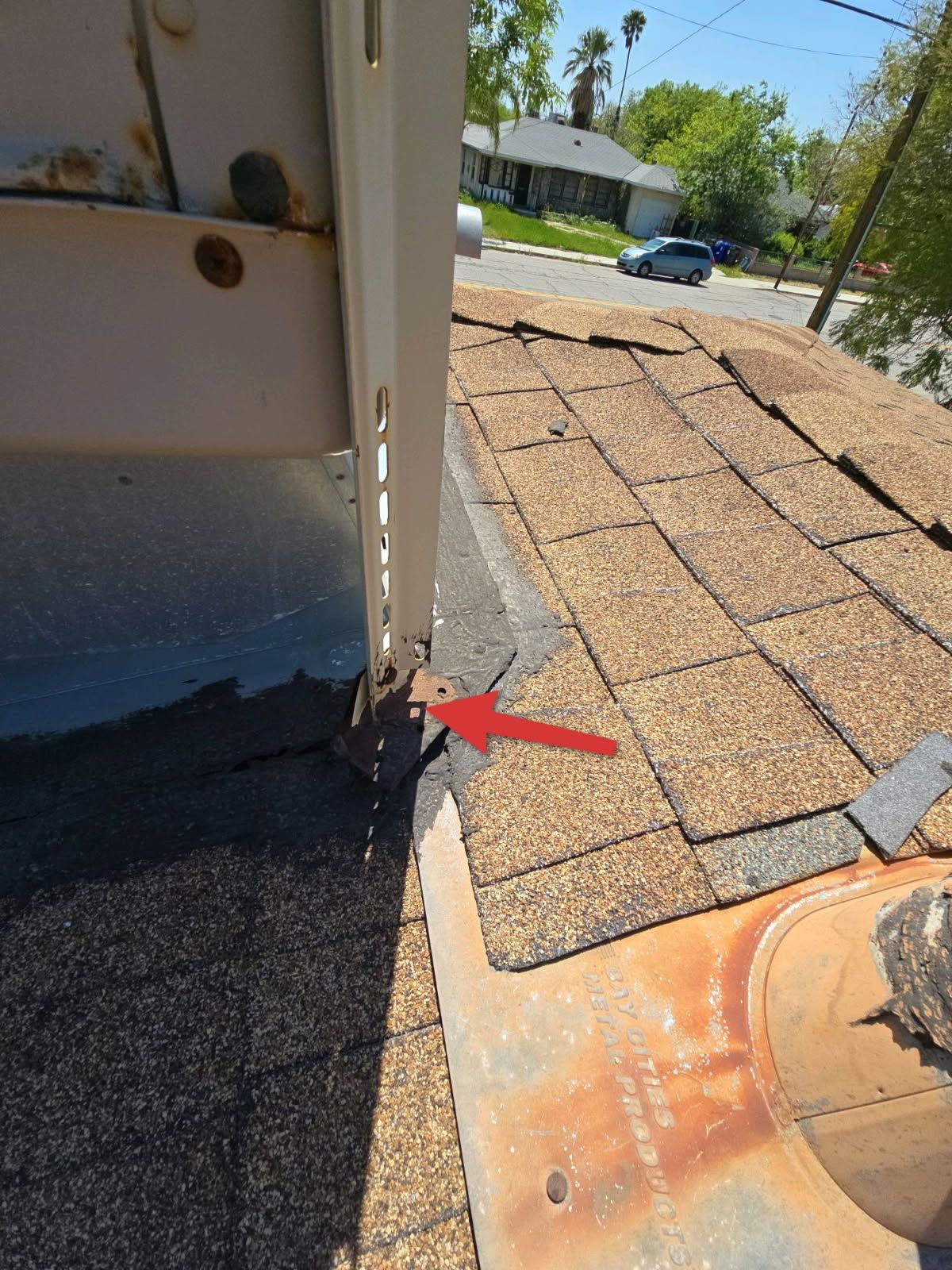 A close-up view of an evaporative cooler on a shingled roof, with a red arrow pointing to a loose mounting bracket base.