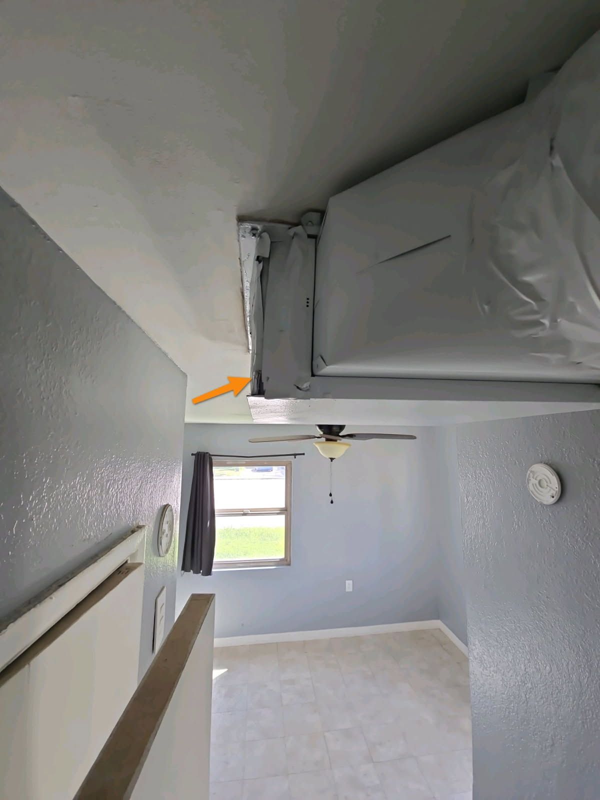 An orange arrow points to an unsealed gap where an HVAC duct meets the ceiling in a room with light blue walls.