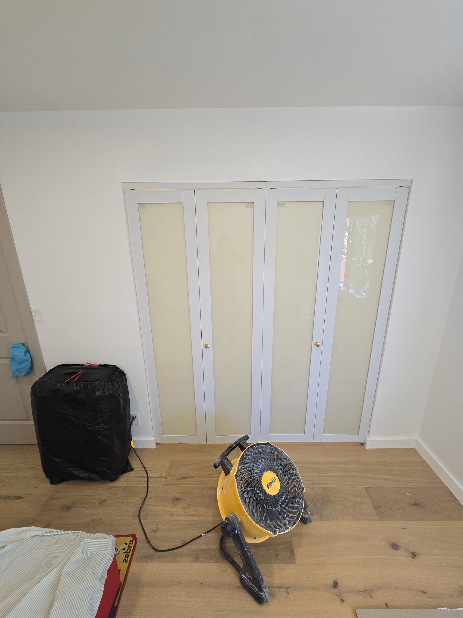 A room with a white folding gate, a black suitcase, and a yellow floor fan on a wooden floor.