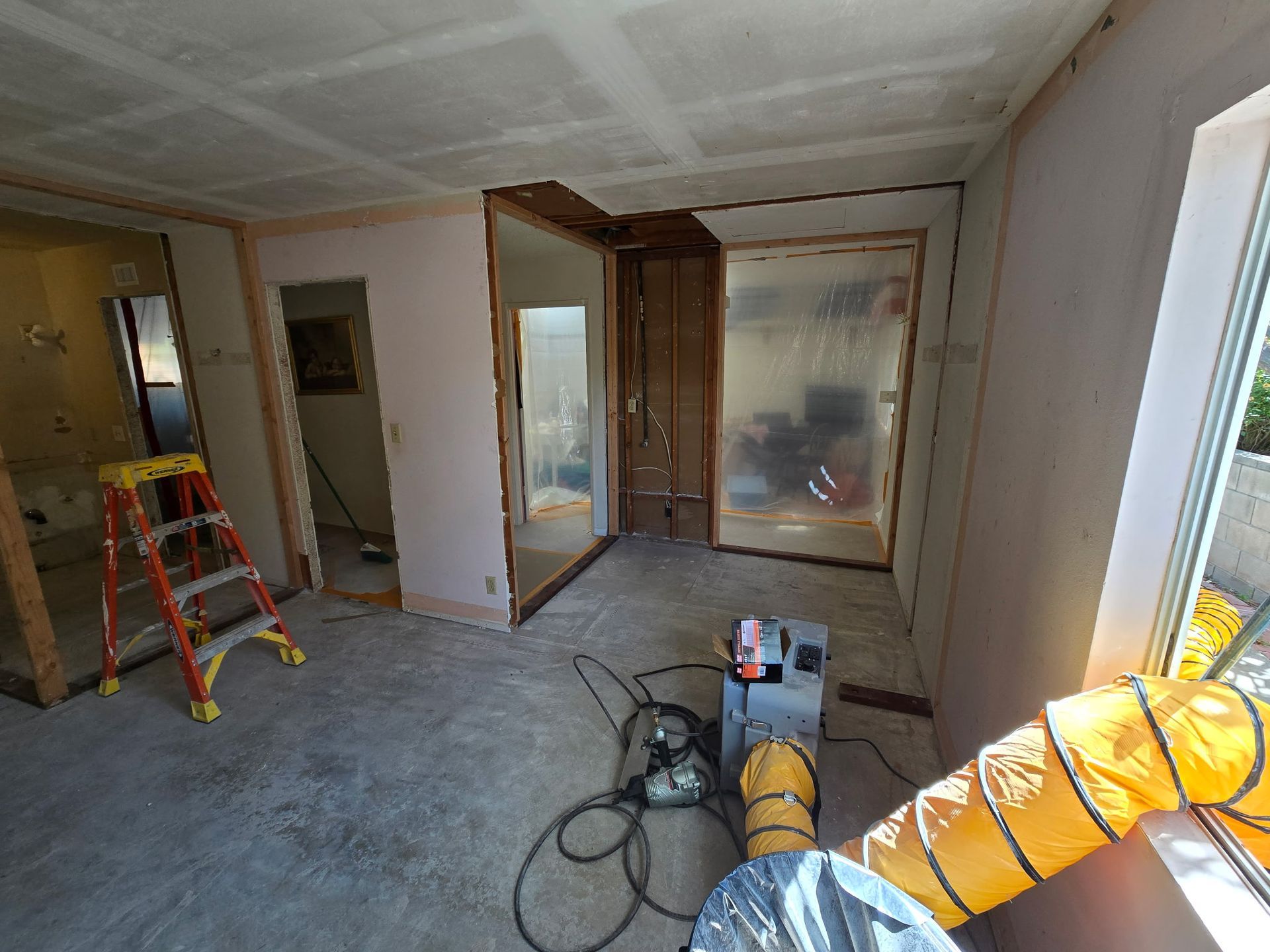 Renovation in progress in a bare room with drywall, ladders, tools, and ventilation hose.