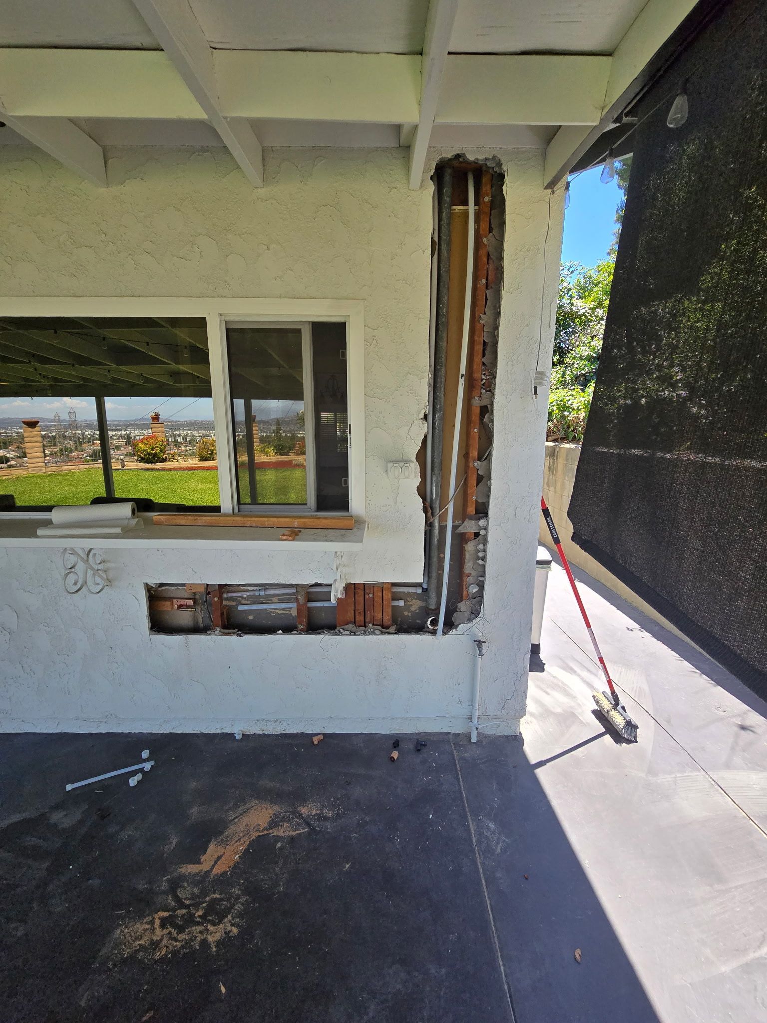Exterior wall under repair beside a window, with exposed framing and dark privacy screen outside.