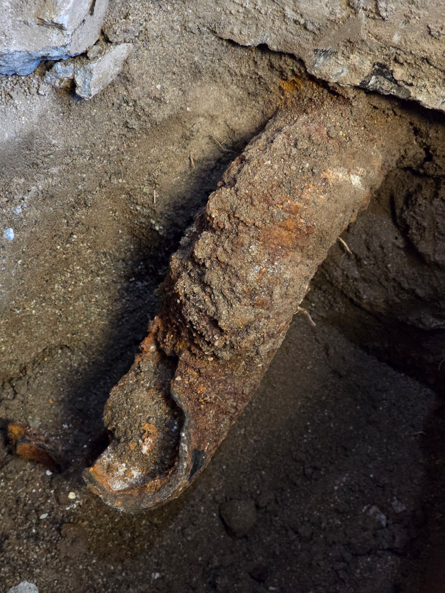 Rusty metal pipe embedded in muddy ground near a wet rock surface