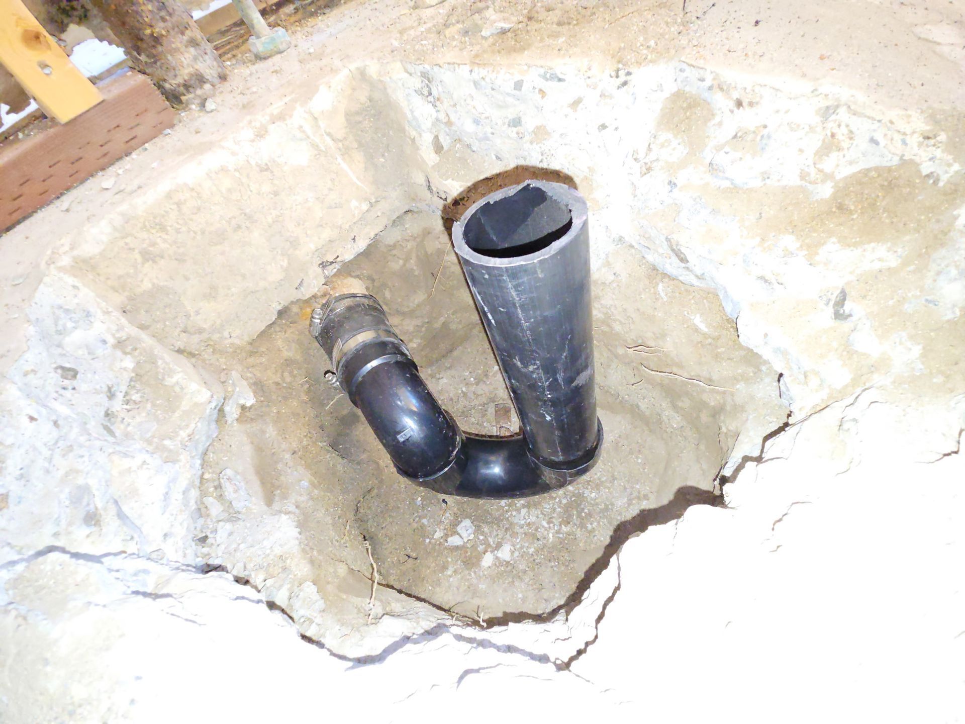Black PVC pipes connected in a rough hole in a concrete floor