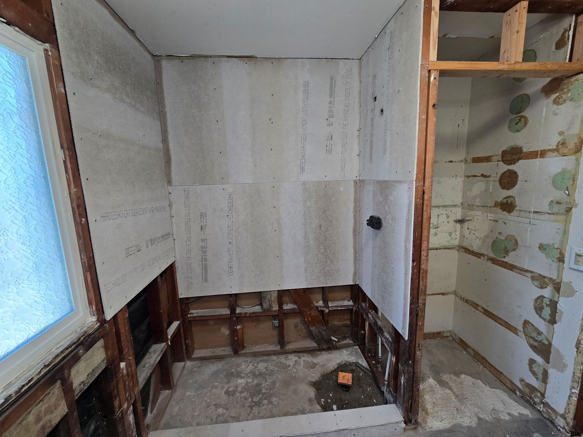 Partially renovated small room with exposed studs, white walls, and a window on the left.