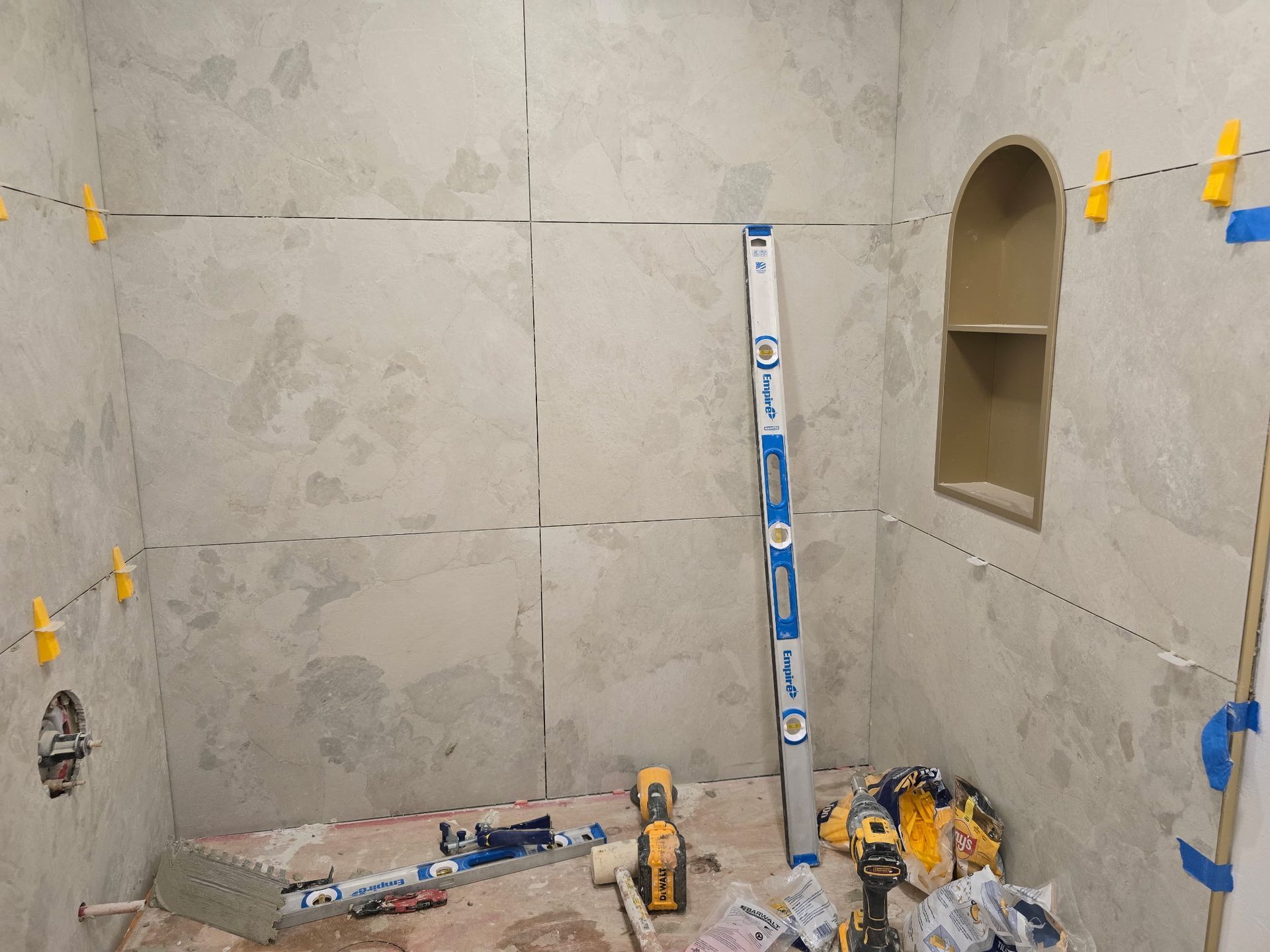 Partially tiled bathroom under construction with tools, tile spacers, and a niche on the right wall