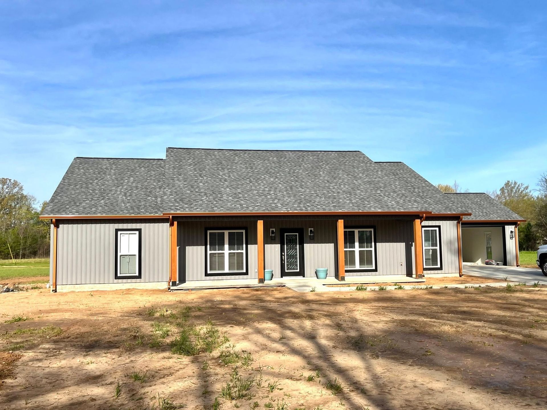 A large house with a gray roof is sitting on top of a dirt field.