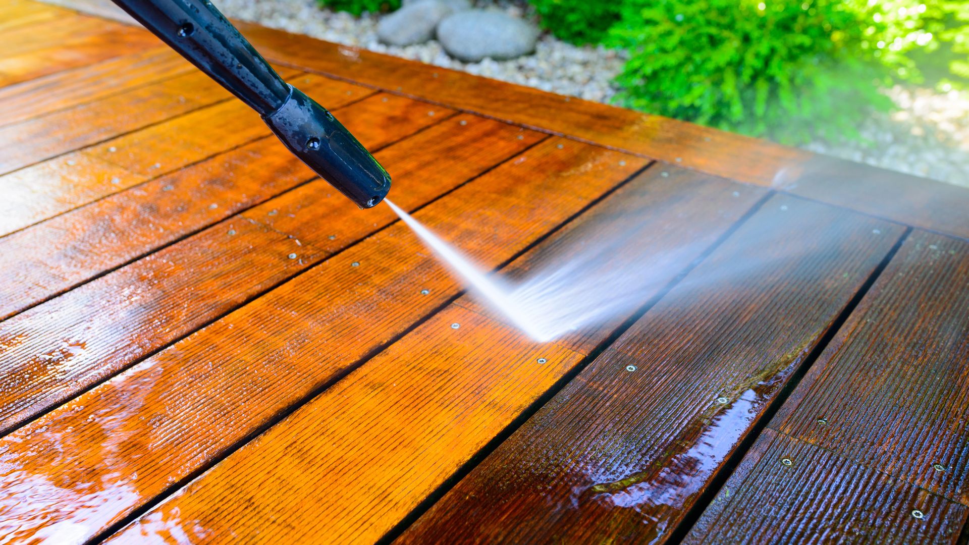 A pressure washer cleaning a weathered wooden deck