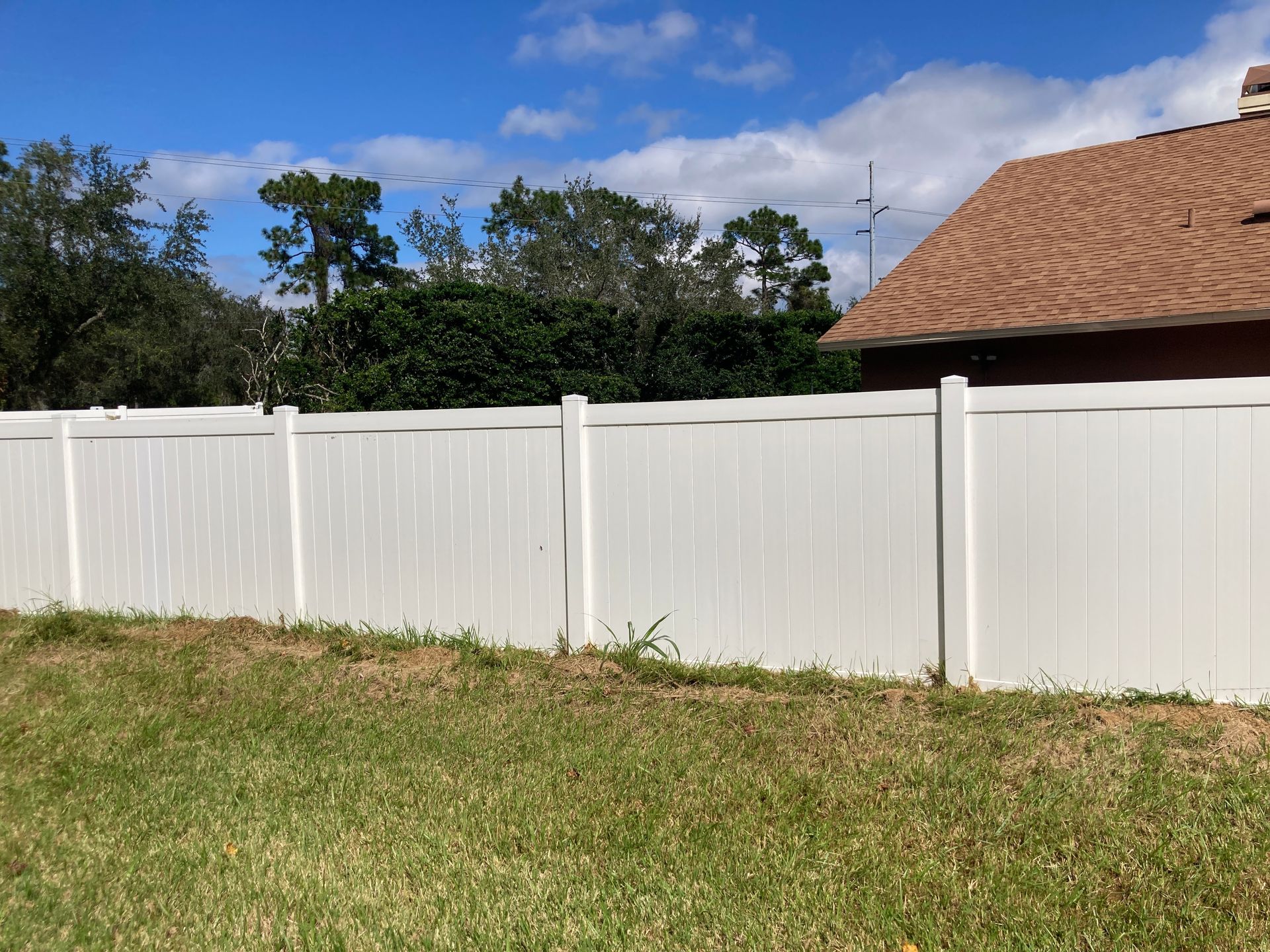 A person uses a pressure washer to clean a brown, corrugated metal fence.