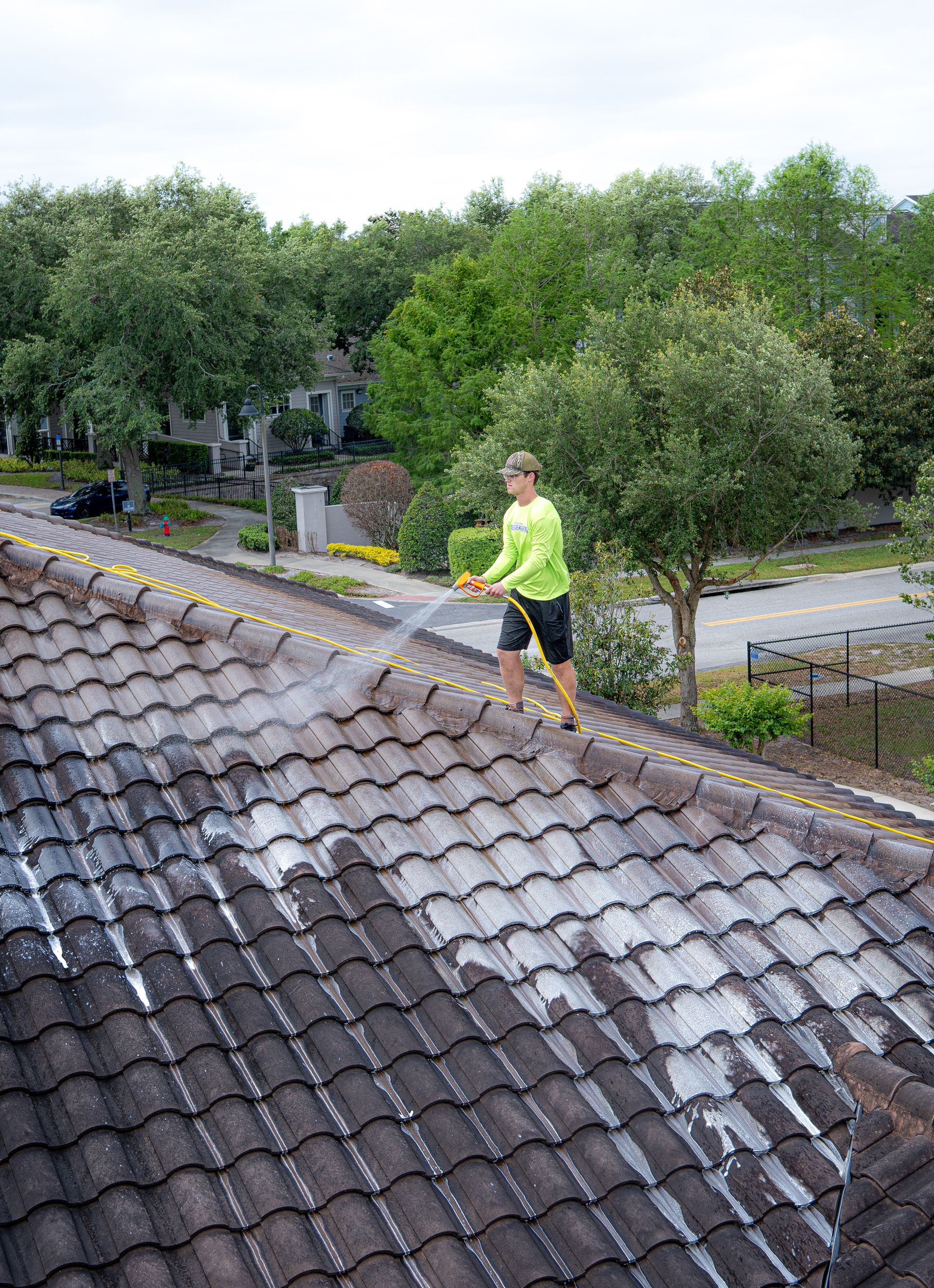 A person wearing jeans and sneakers uses a pressure washer to clean red roof tiles.