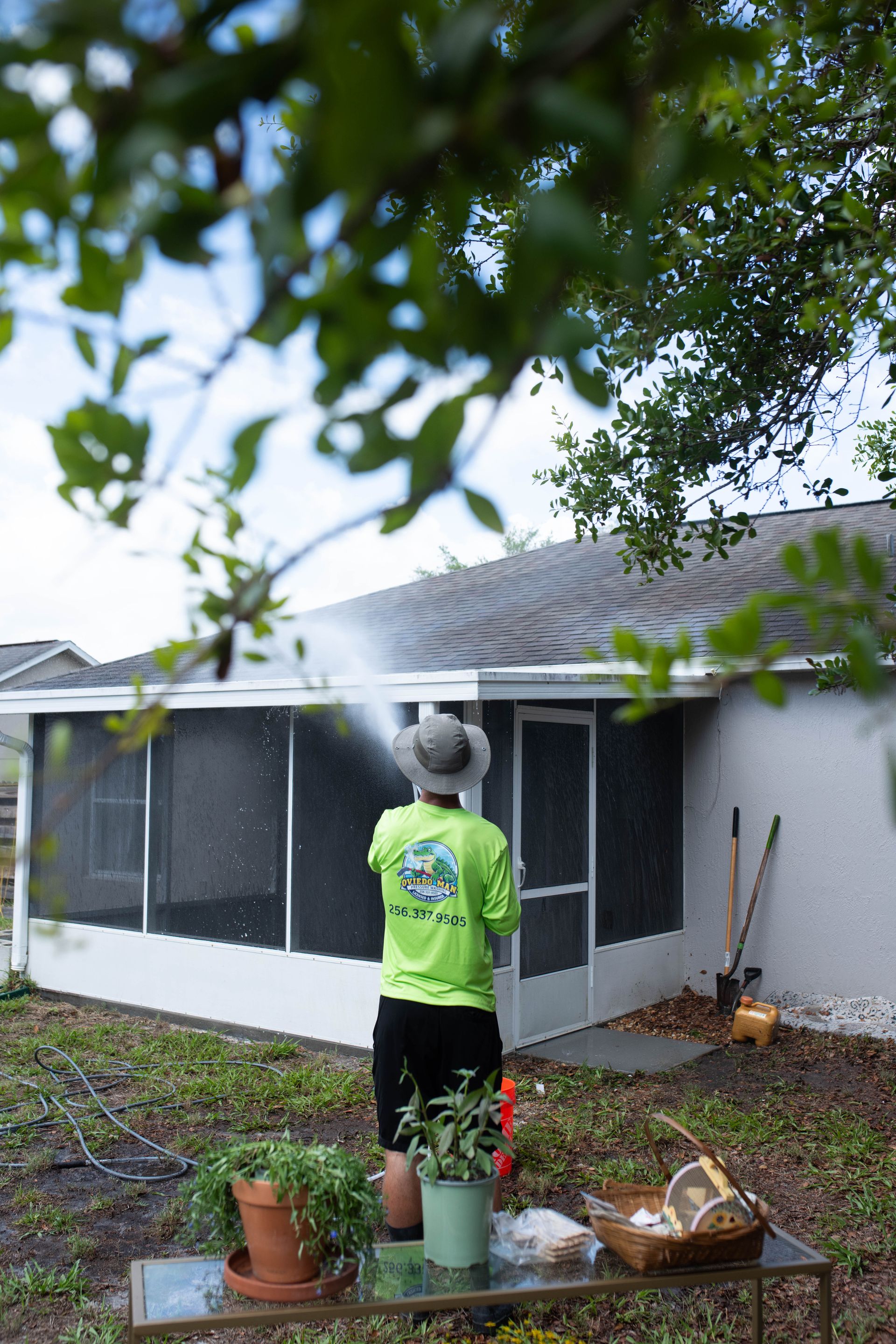 A person uses a pressure washer to clean a wooden deck outdoors, spraying a stream of water across the wood planks.