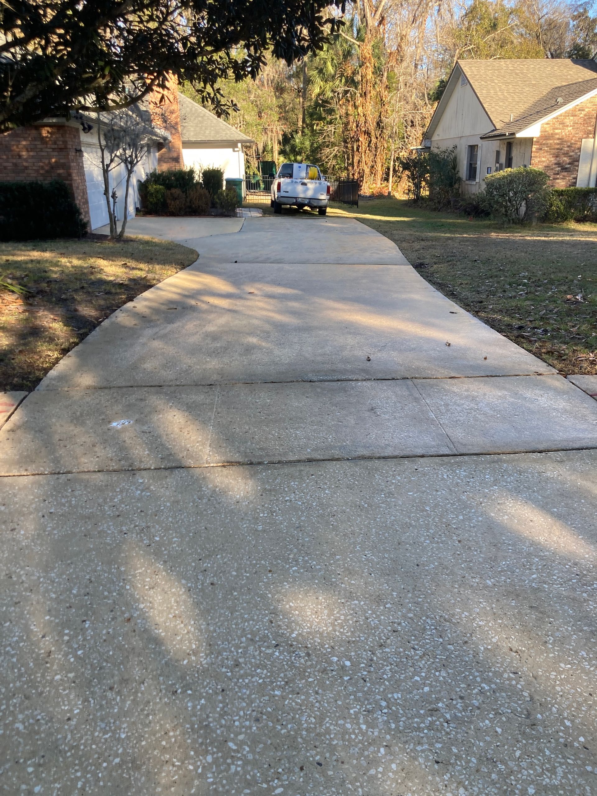 A paved residential driveway leads toward a white truck parked between two houses on a sunny, leaf-strewn day.