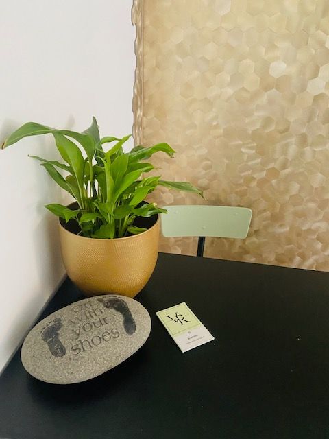 Een groene potplant, een grijze stenen onderzetter en een klein kaartje op een zwarte tafel naast een muur met structuurverf.