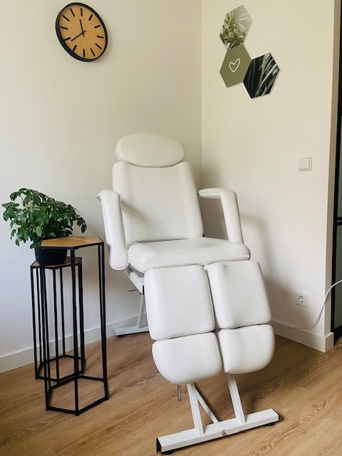 Witte relaxfauteuil in een kamer met een potplant, een wandklok en geometrische muurdecoratie, op een houten vloer.