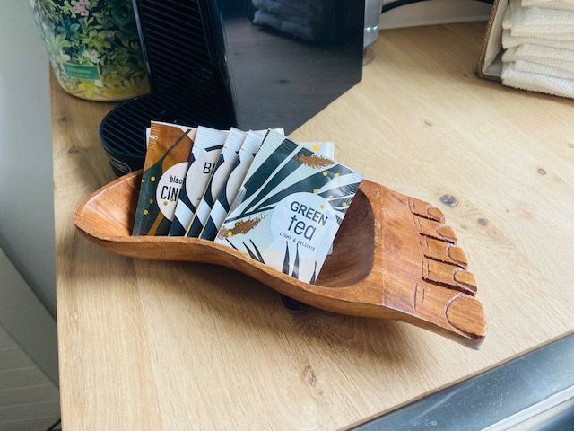 Een houten dienblad met meerdere theepakjes op een lichte houten tafel.