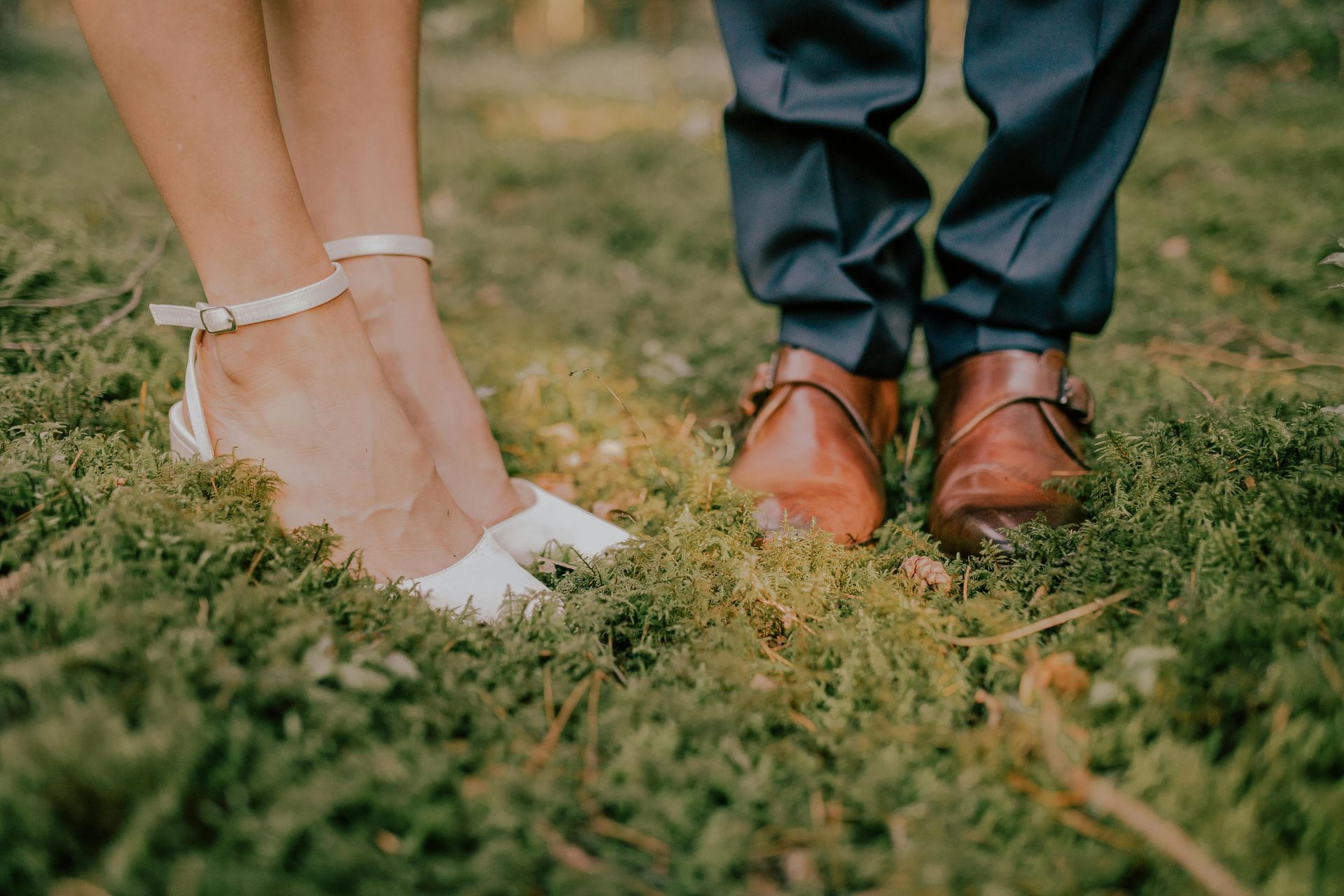 De voeten van het bruidspaar in het gras, met witte hakken en bruine nette schoenen.