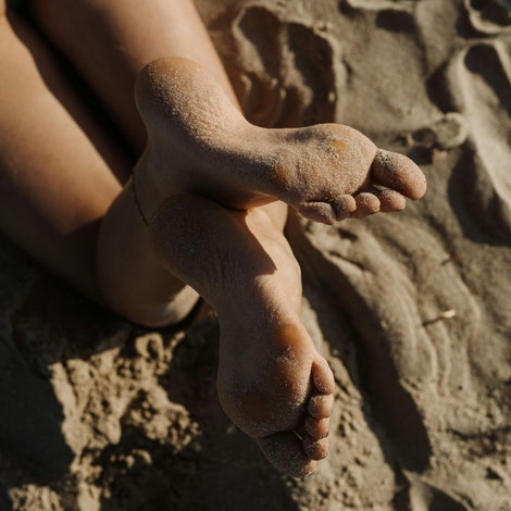 Blote voeten, bedekt met zand, rustend op een zandstrand.