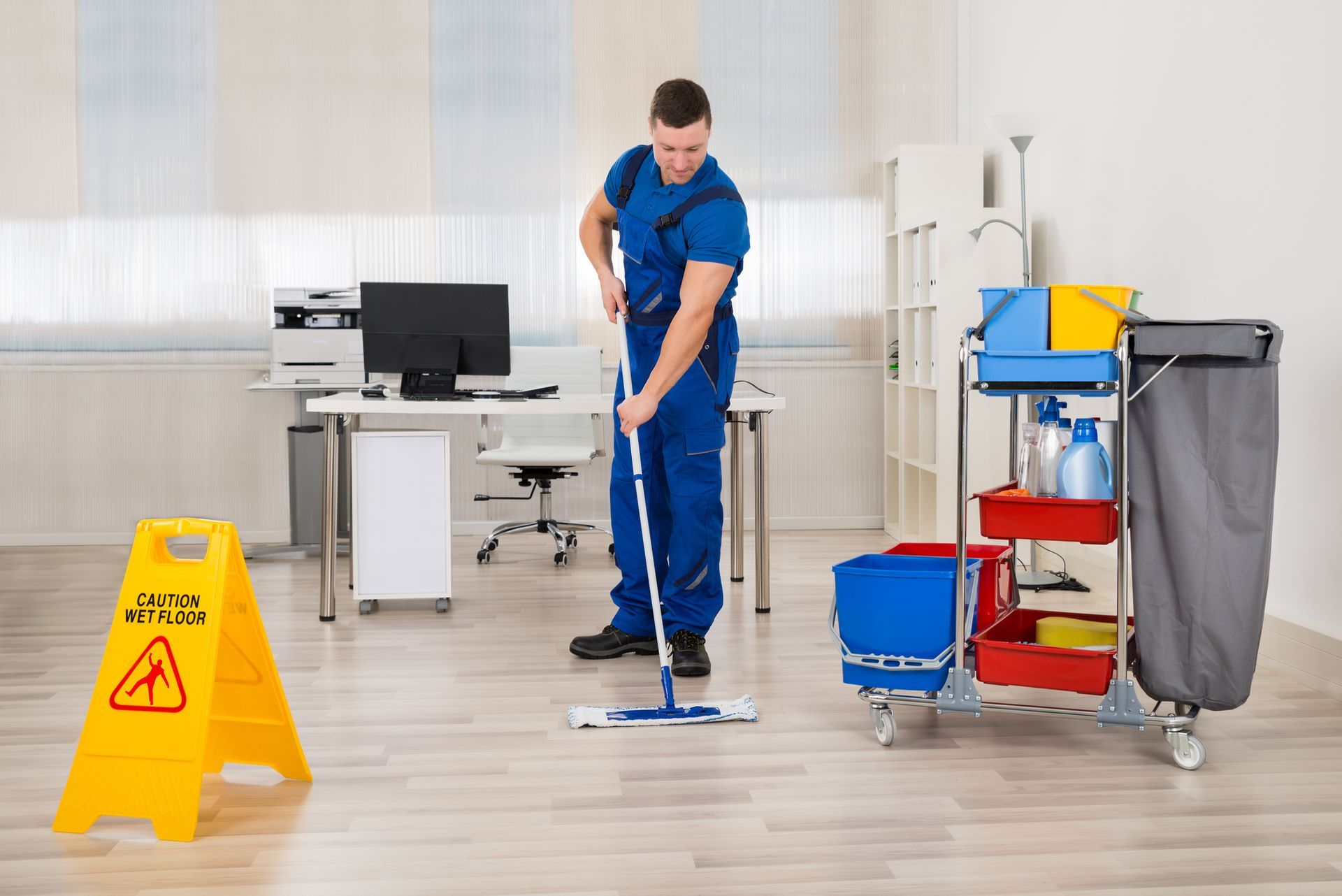 A man is mopping the floor in an office next to a caution sign – Lake Worth, FL – FL Cleaning Services