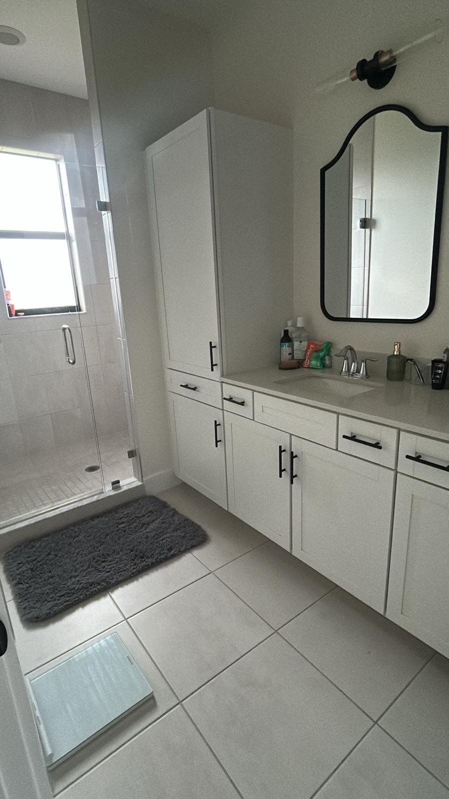 A bathroom with white cabinets , a sink , a mirror and a walk in shower.