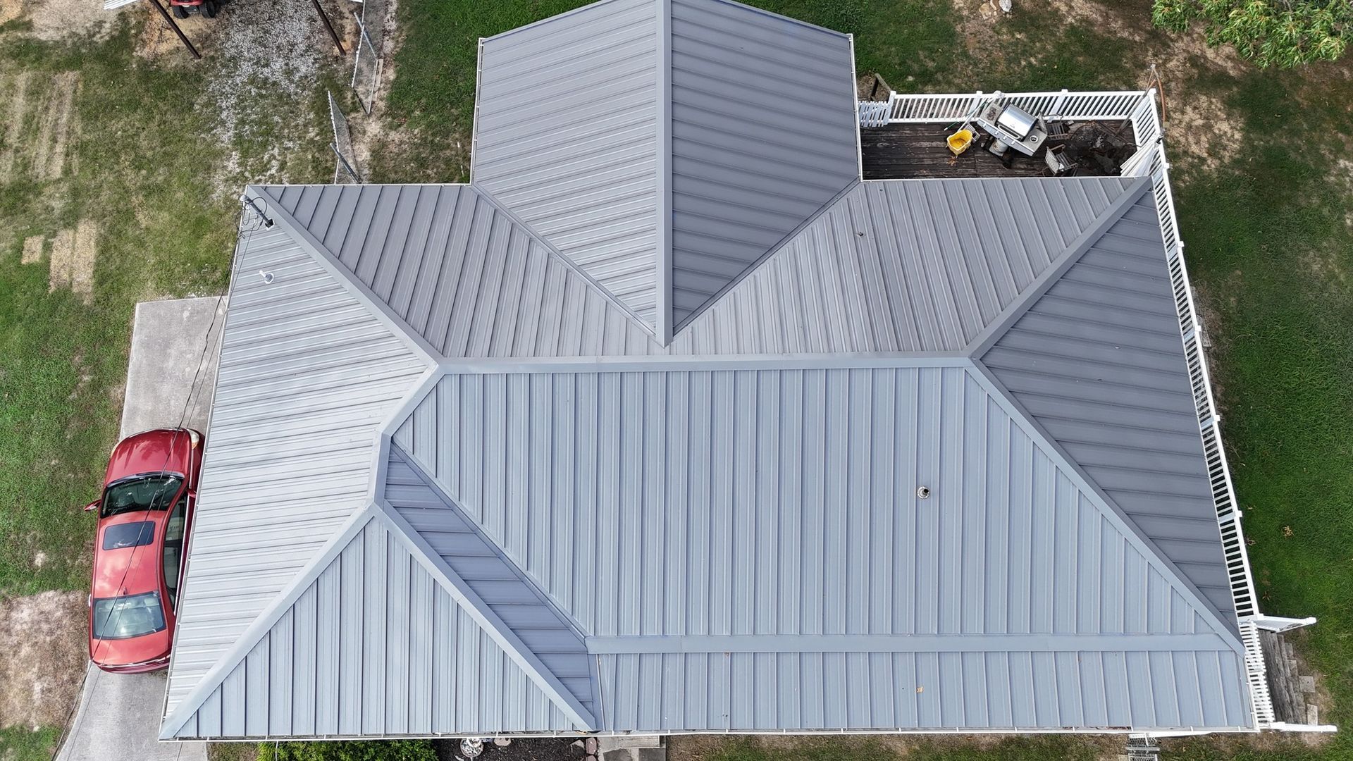 An aerial view of a house with a metal roof and a red car parked in front of it.