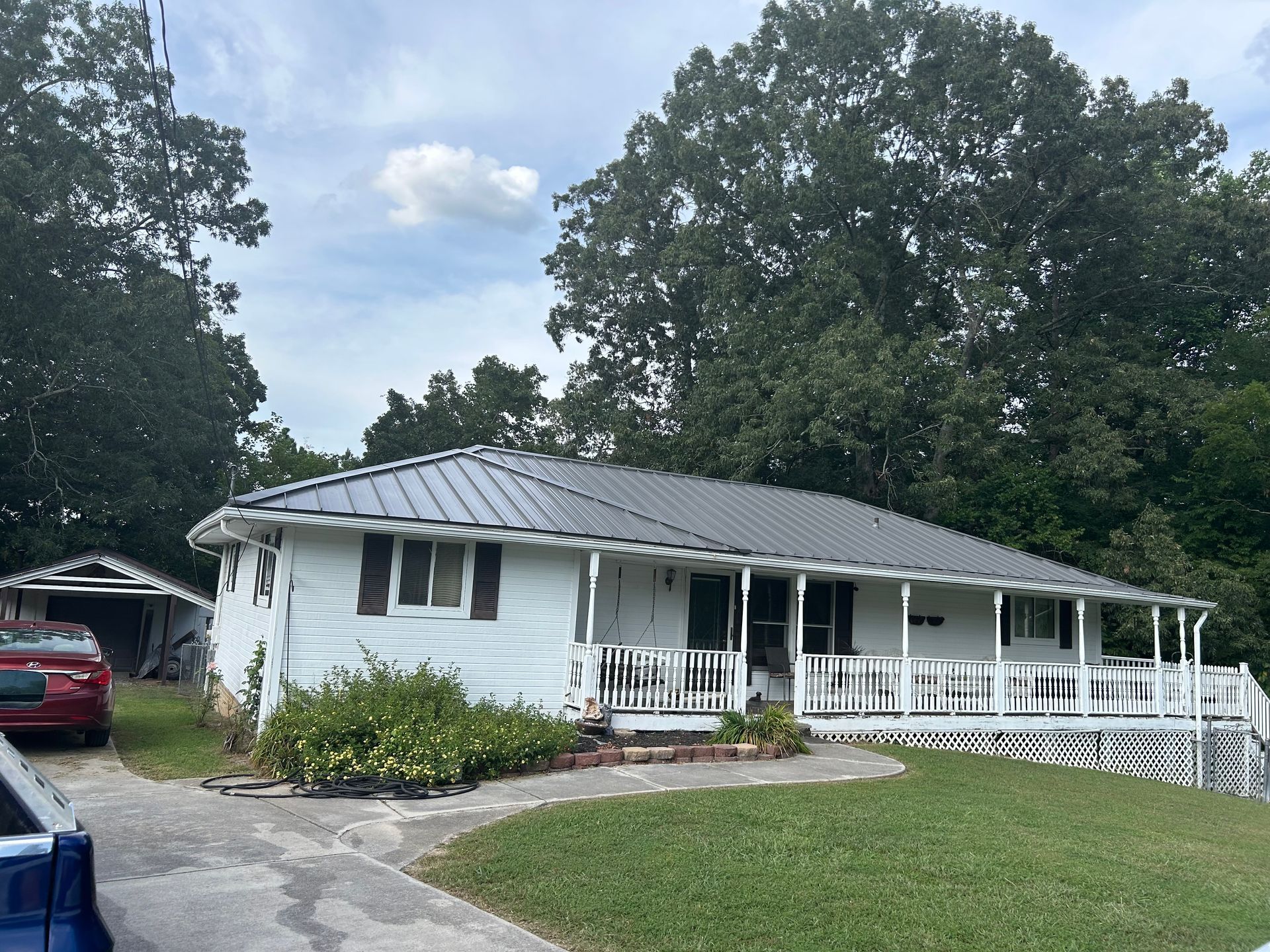 A white house with a metal roof and a porch is surrounded by trees.