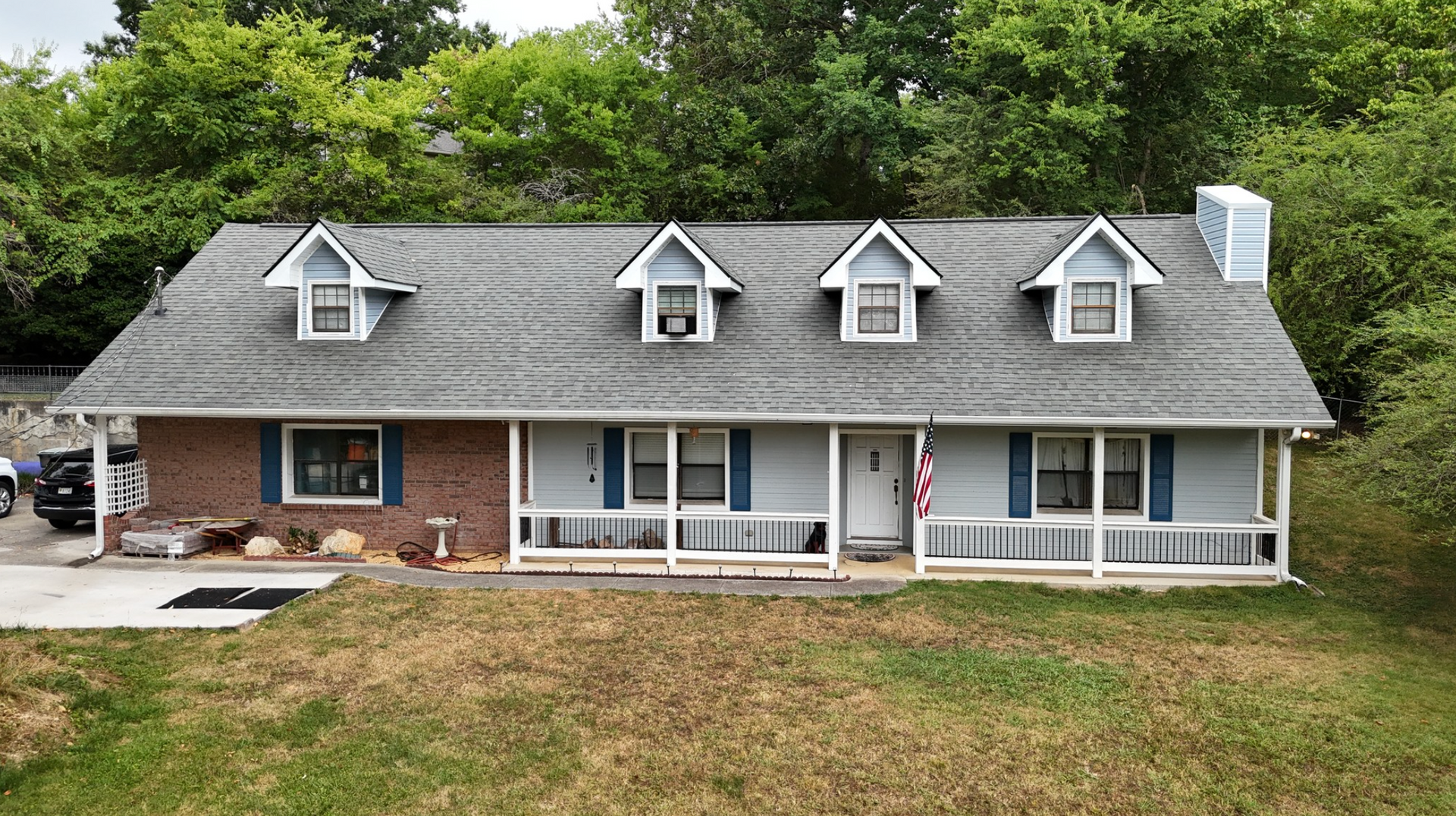 A brick house with a blue porch and a gray roof surrounded by trees.