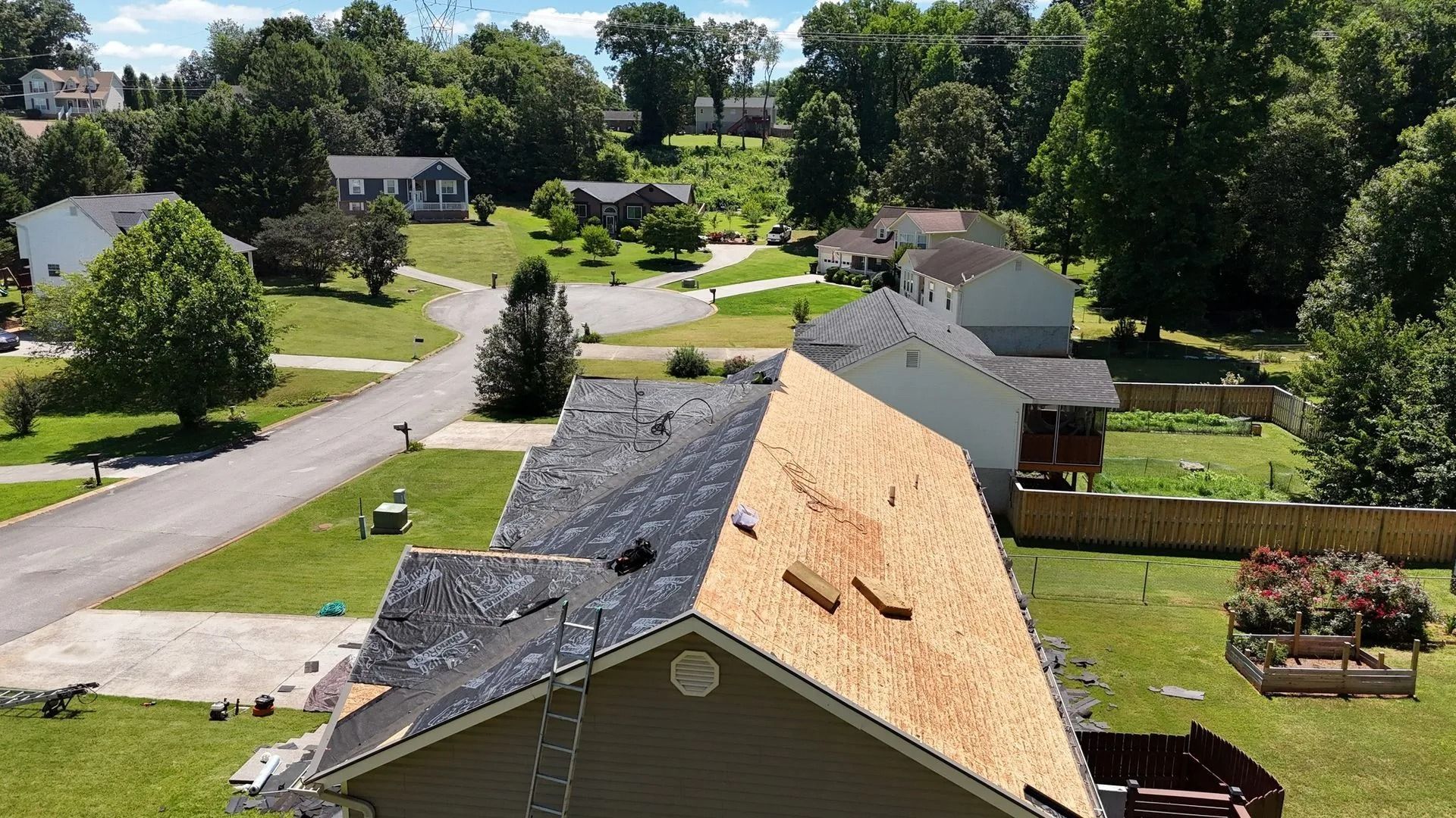 Aerial view of a house with half of the roof shingles removed, revealing the wood frame.