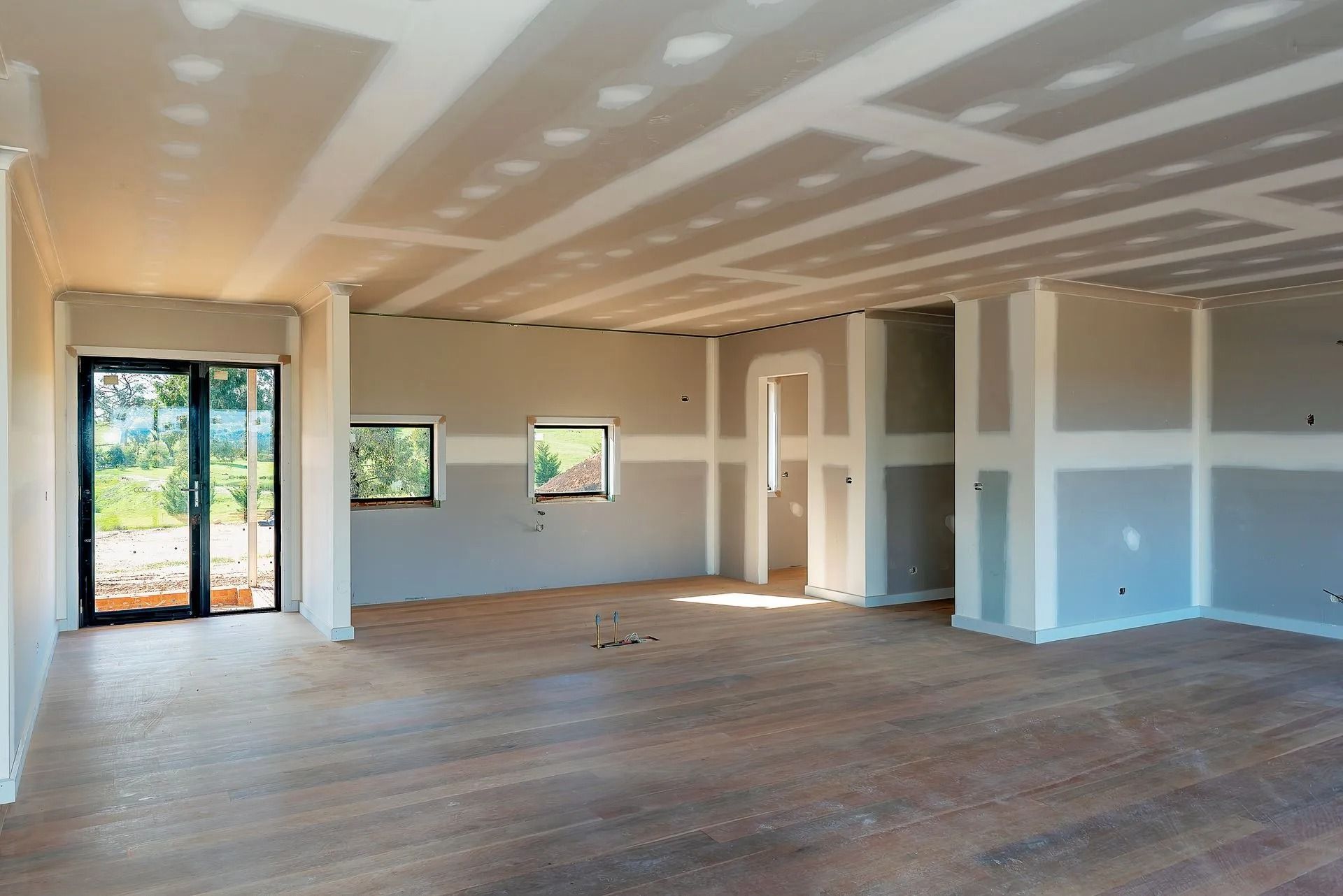 Interior view of a room under construction, with exposed drywall and wood flooring.