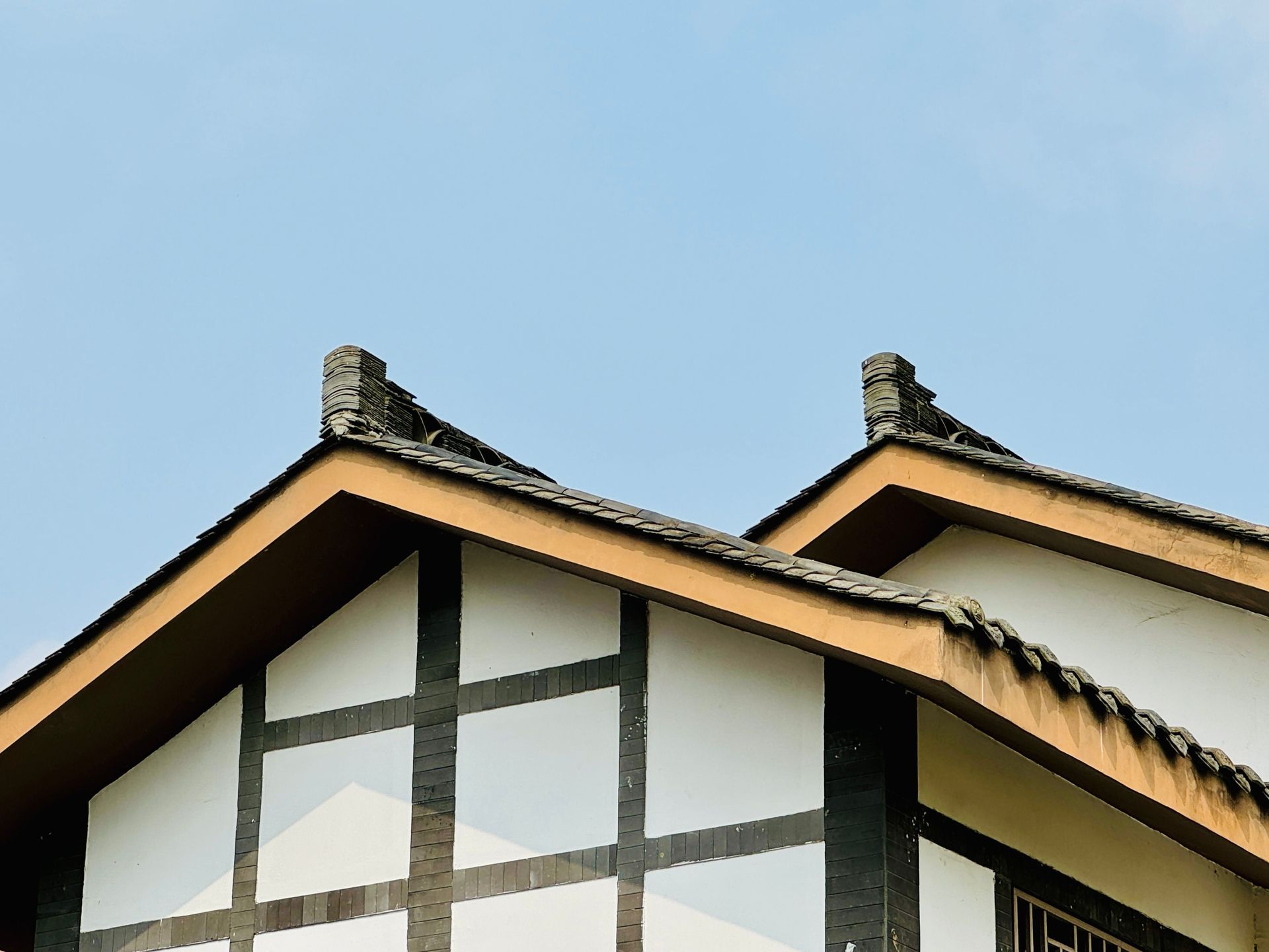 Gabled house roof with dark beams and stone chimneys against a blue sky