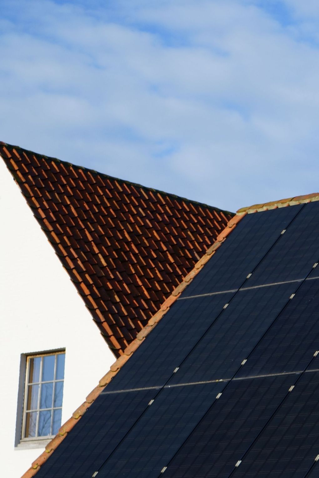Solar panels on a rooftop beside a triangular red-tiled roof under a blue sky.