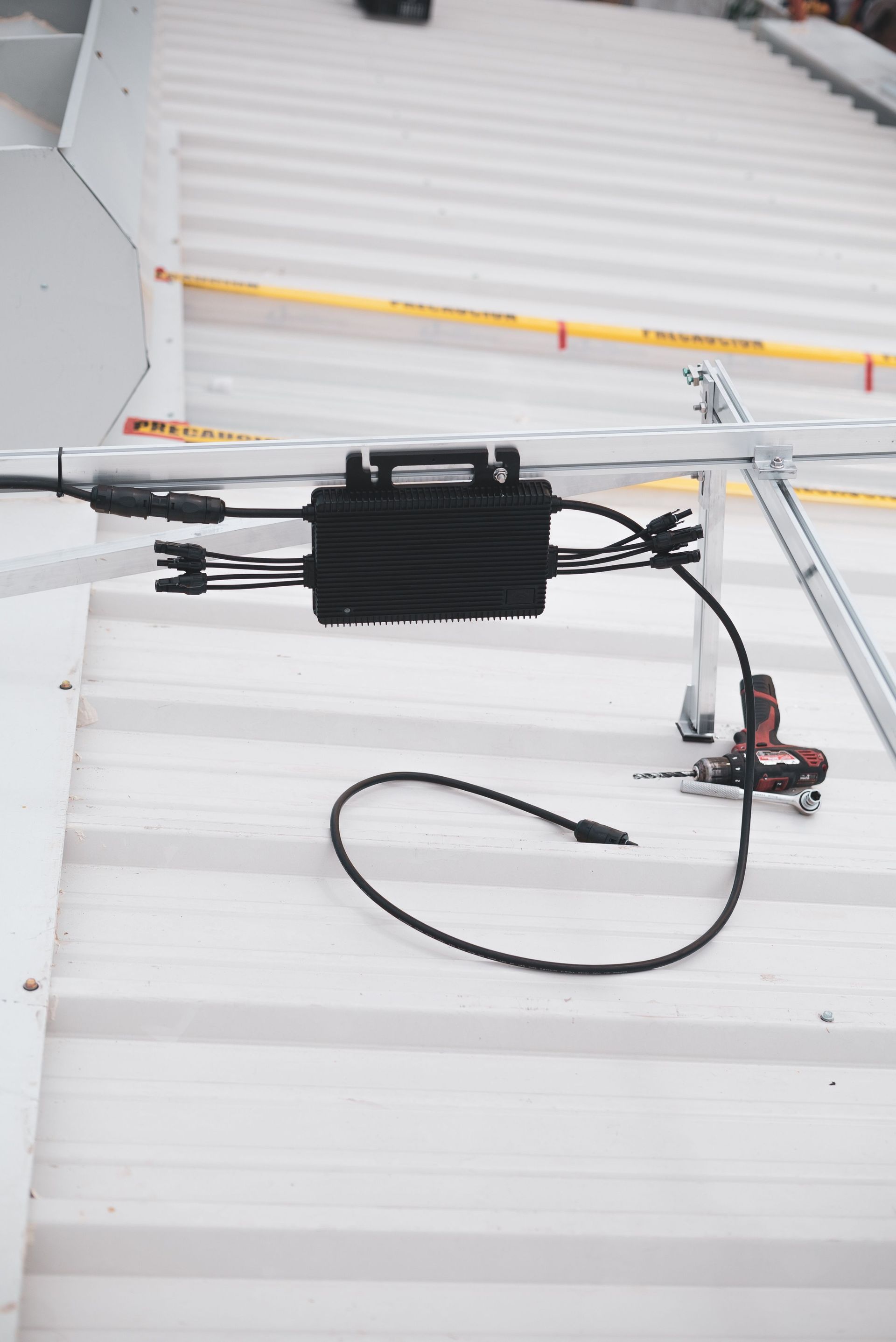 Black electric device and coiled cable mounted on a white corrugated wall outdoors.